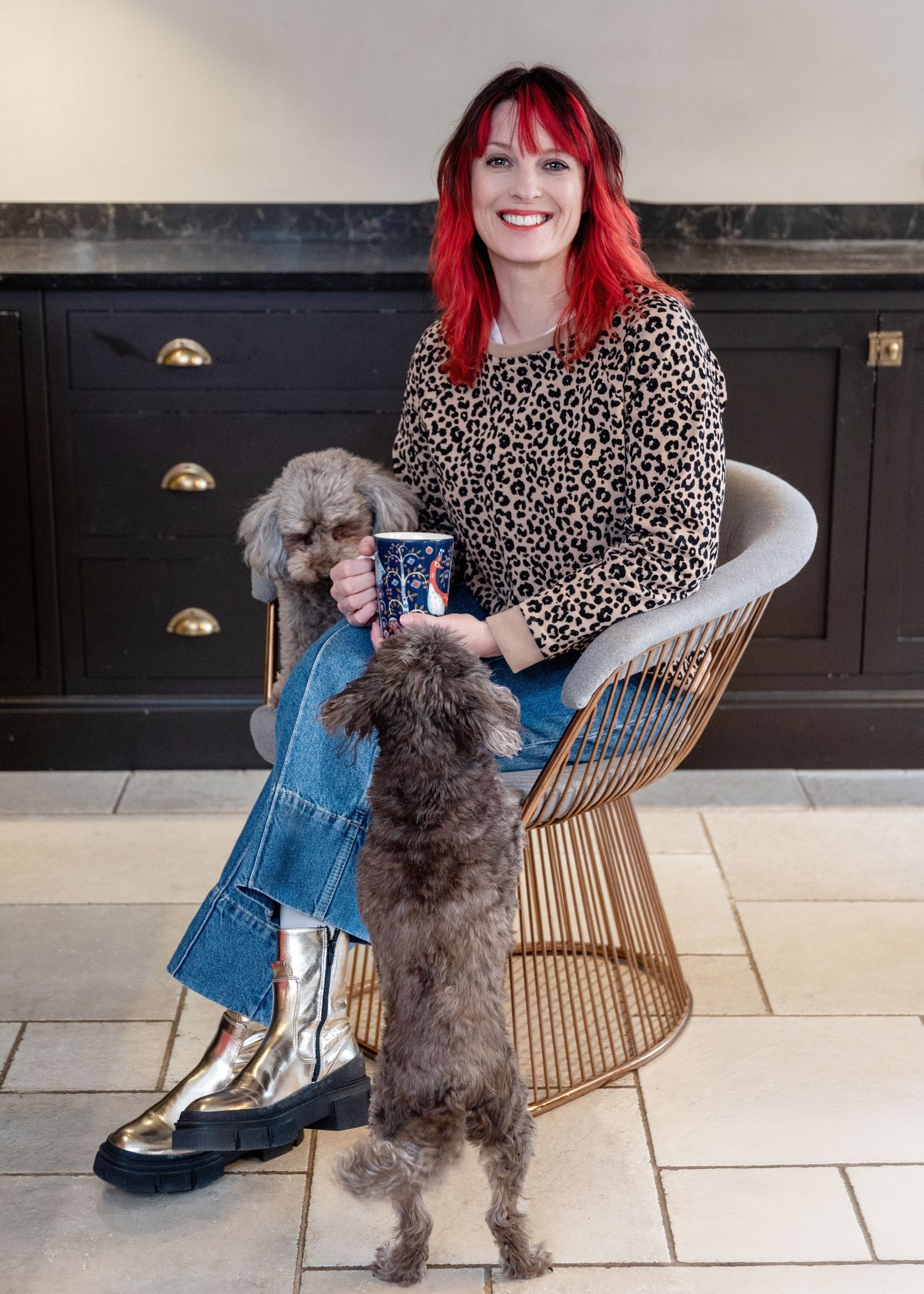 A person wearing a leopard print sweater sits in a modern chair while a fluffy gray dog stands up on their legs.