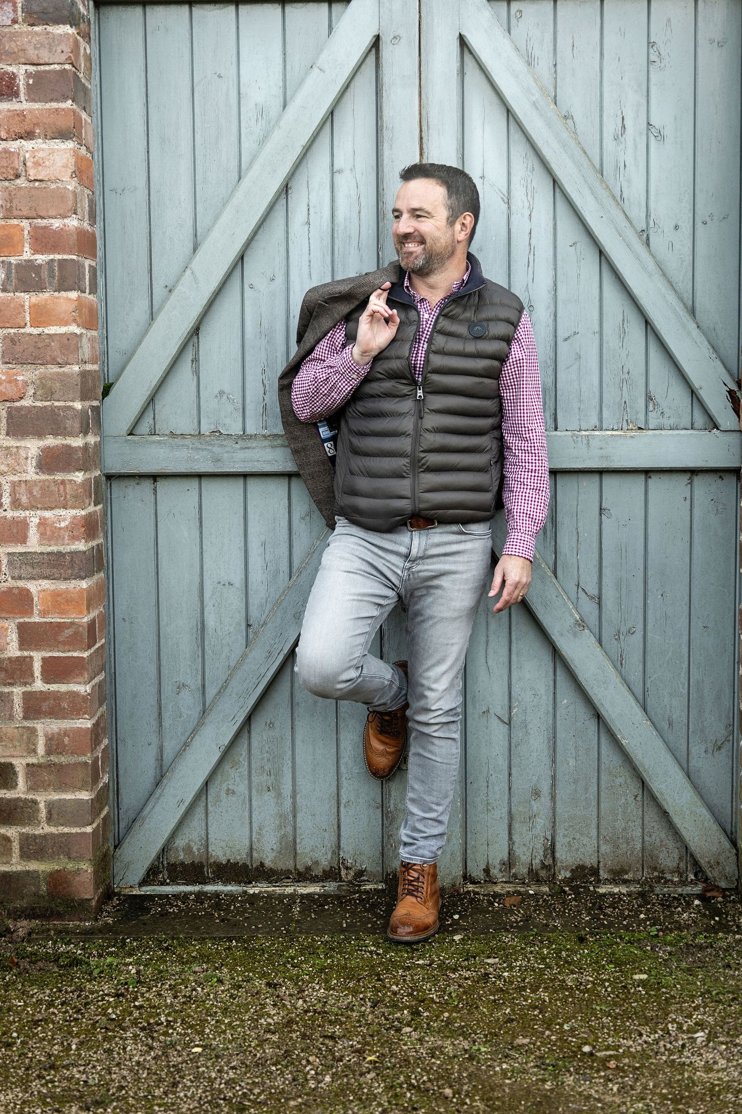 Casual portrait of person wearing black quilted vest and purple shirt leaning against blue barn door.