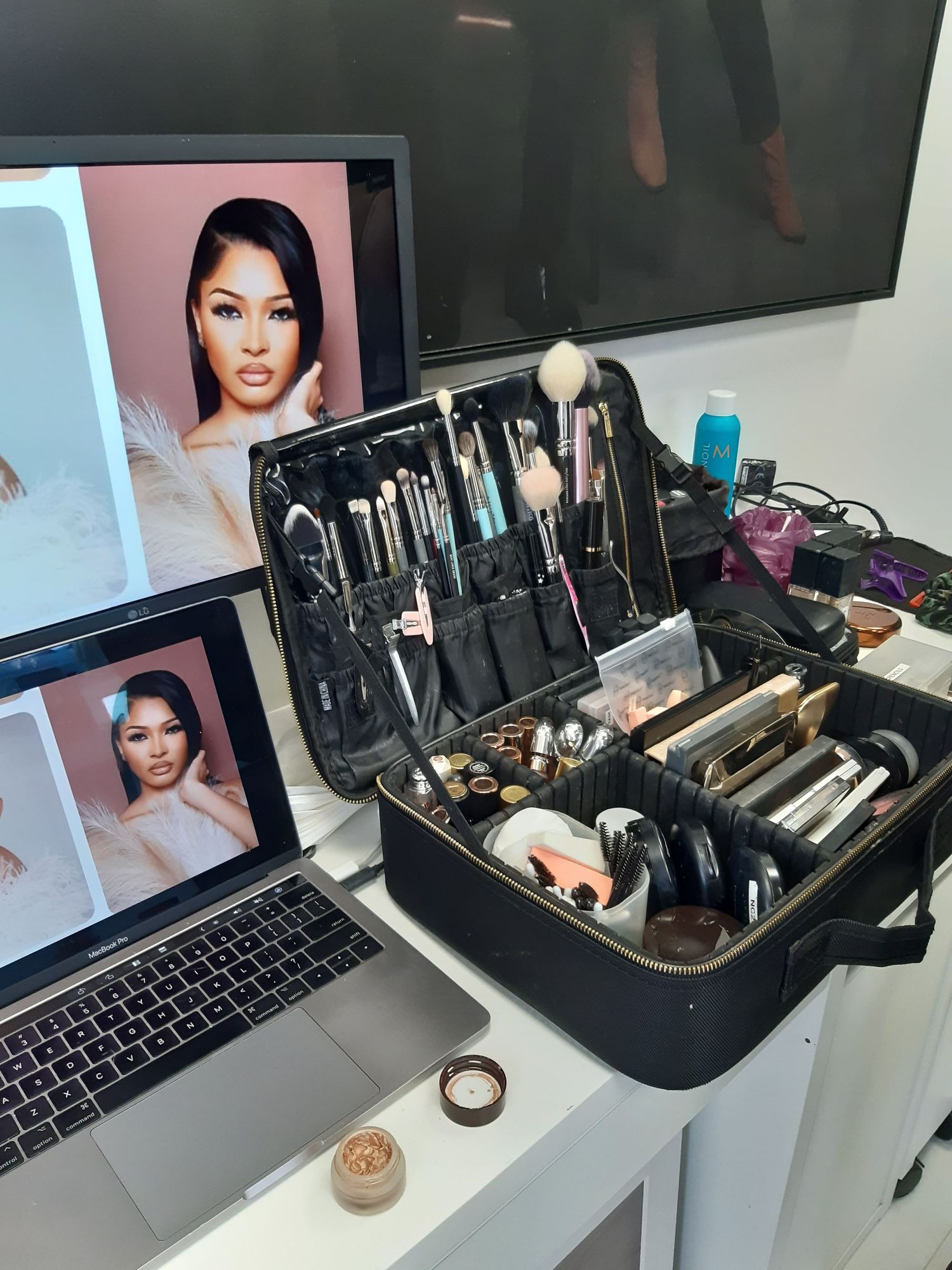 Makeup station with professional brushes, laptop and cosmetics laid out on white desk.