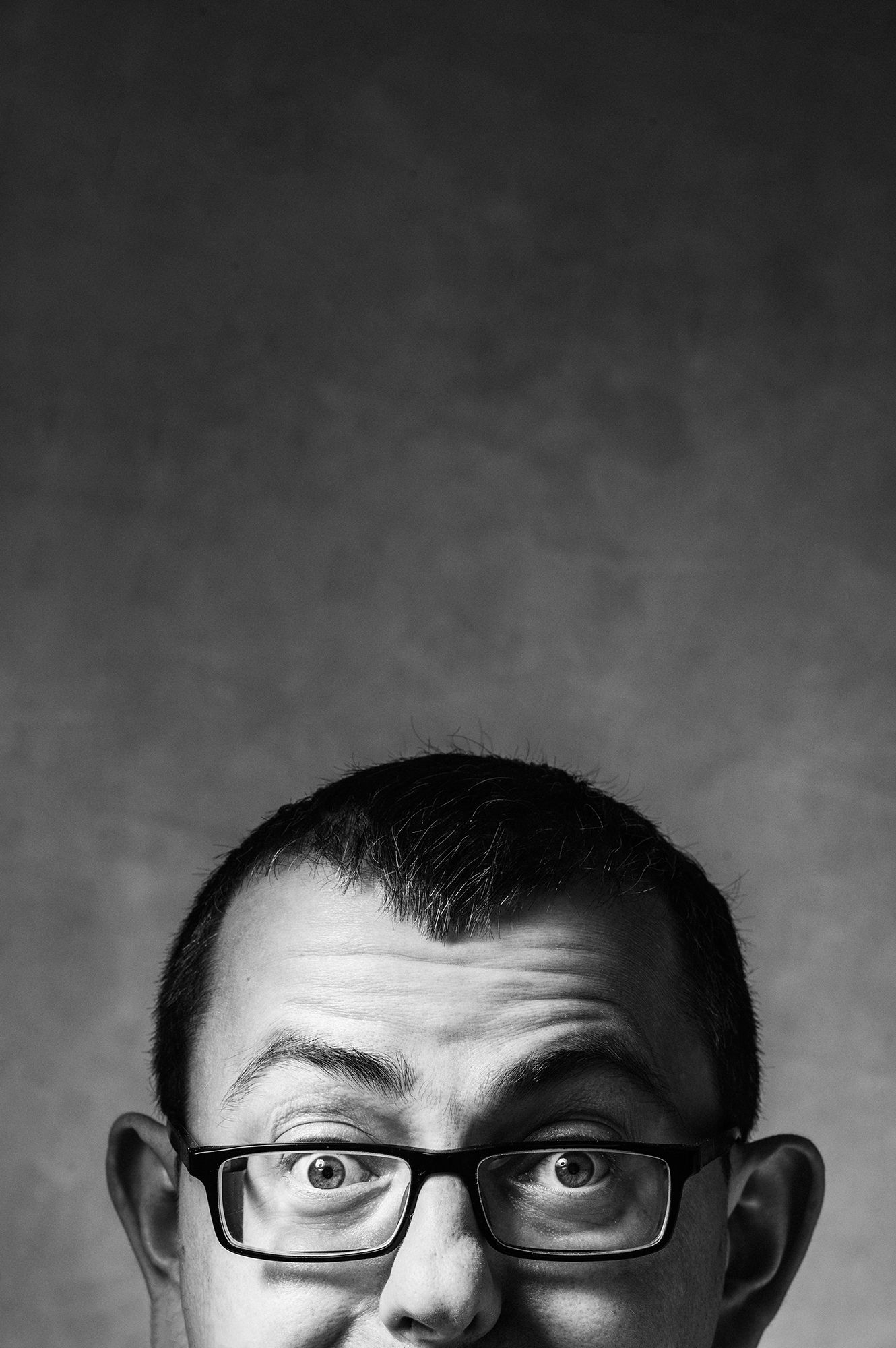 Close-up black and white portrait of person wearing glasses looking up with wide eyes.