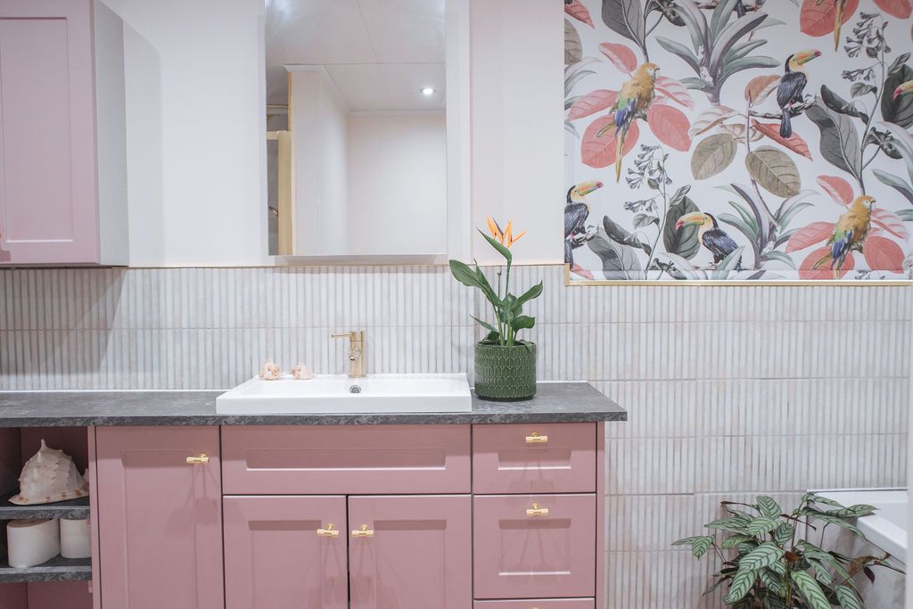 Modern pink kitchen interior with floral wallpaper, white cabinets, and gold hardware accents creates an elegant design scheme.