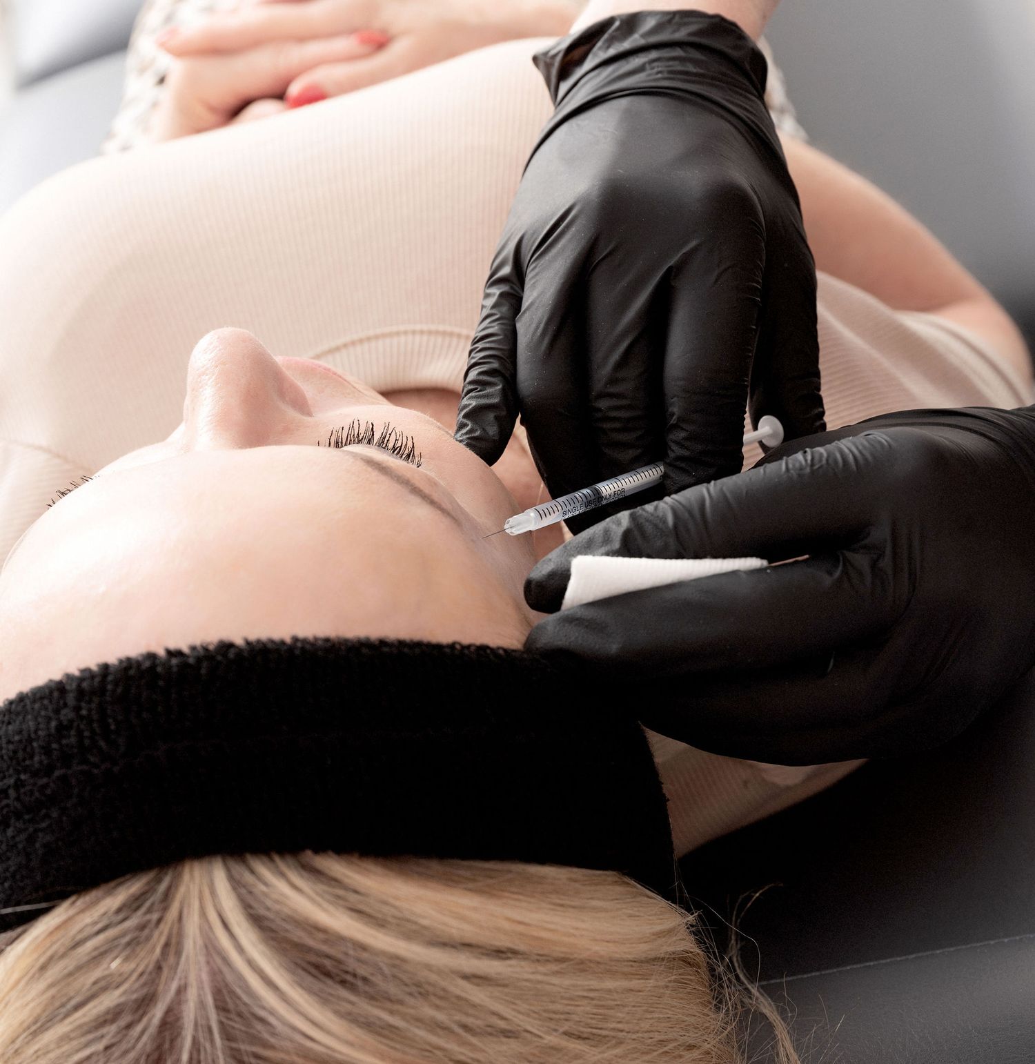 Close-up of an aesthetic treatment being performed with black gloved hands.