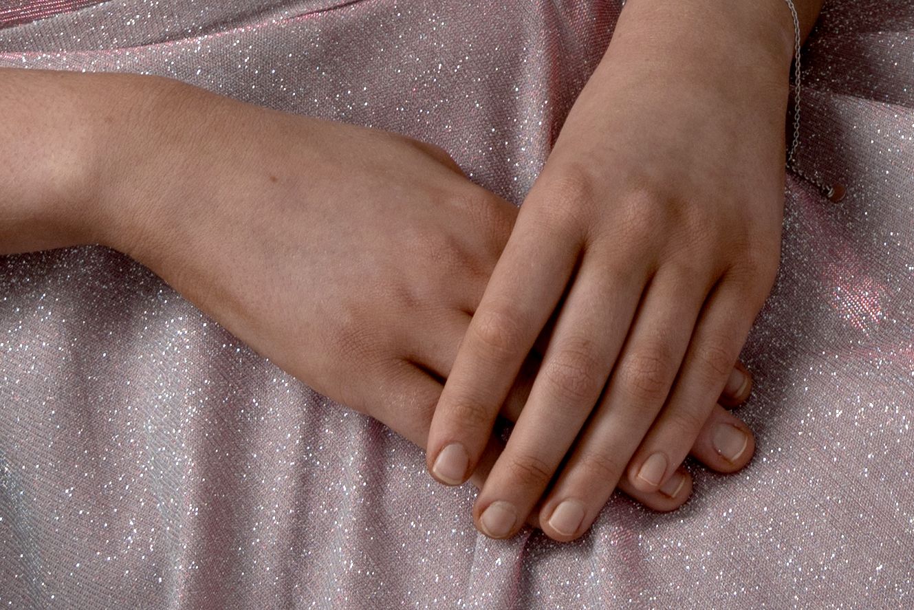 Hands gently resting on sparkly pink fabric creating an elegant composition.