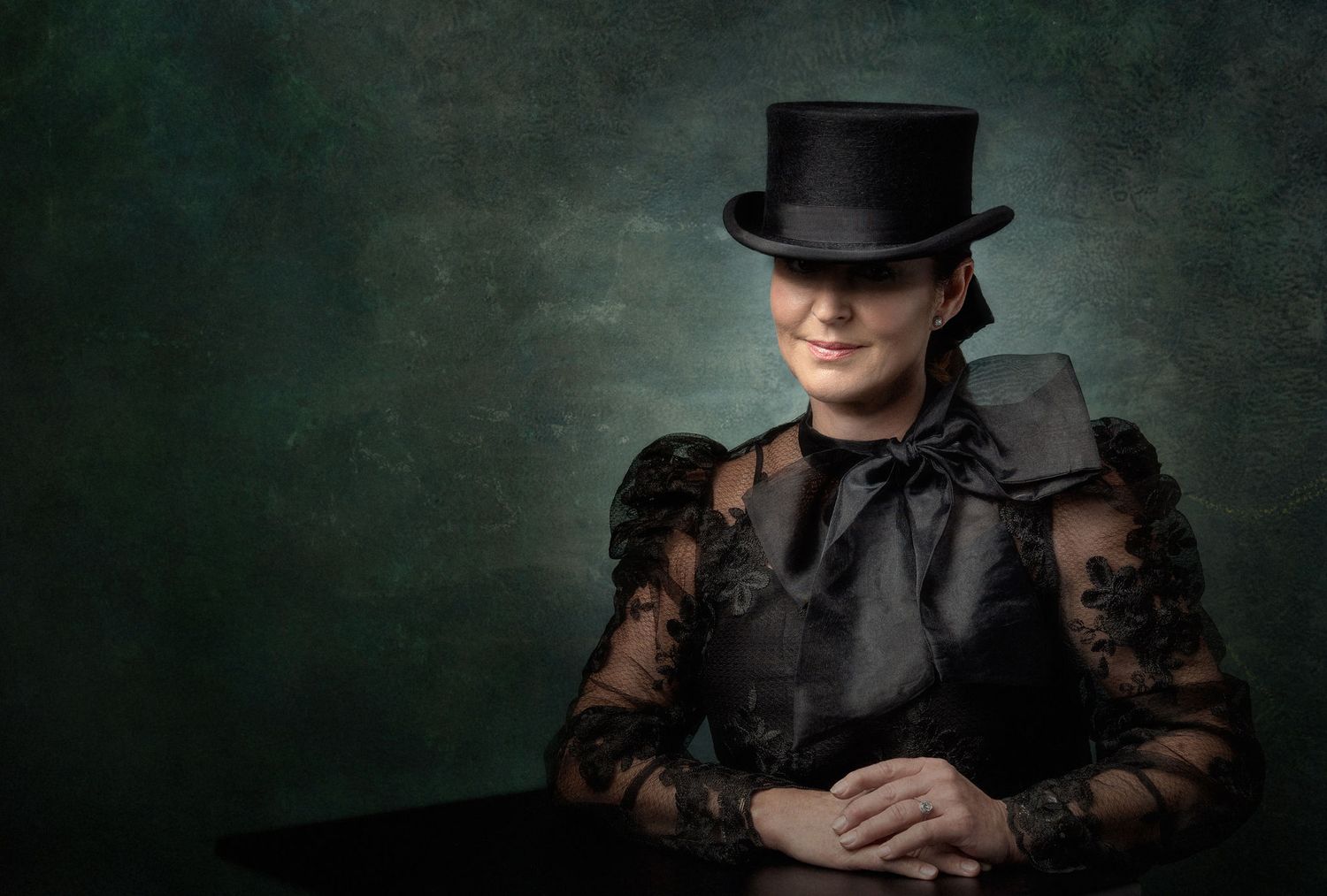 Dramatic portrait of a figure in a top hat and lace sleeves against a dark moody background.