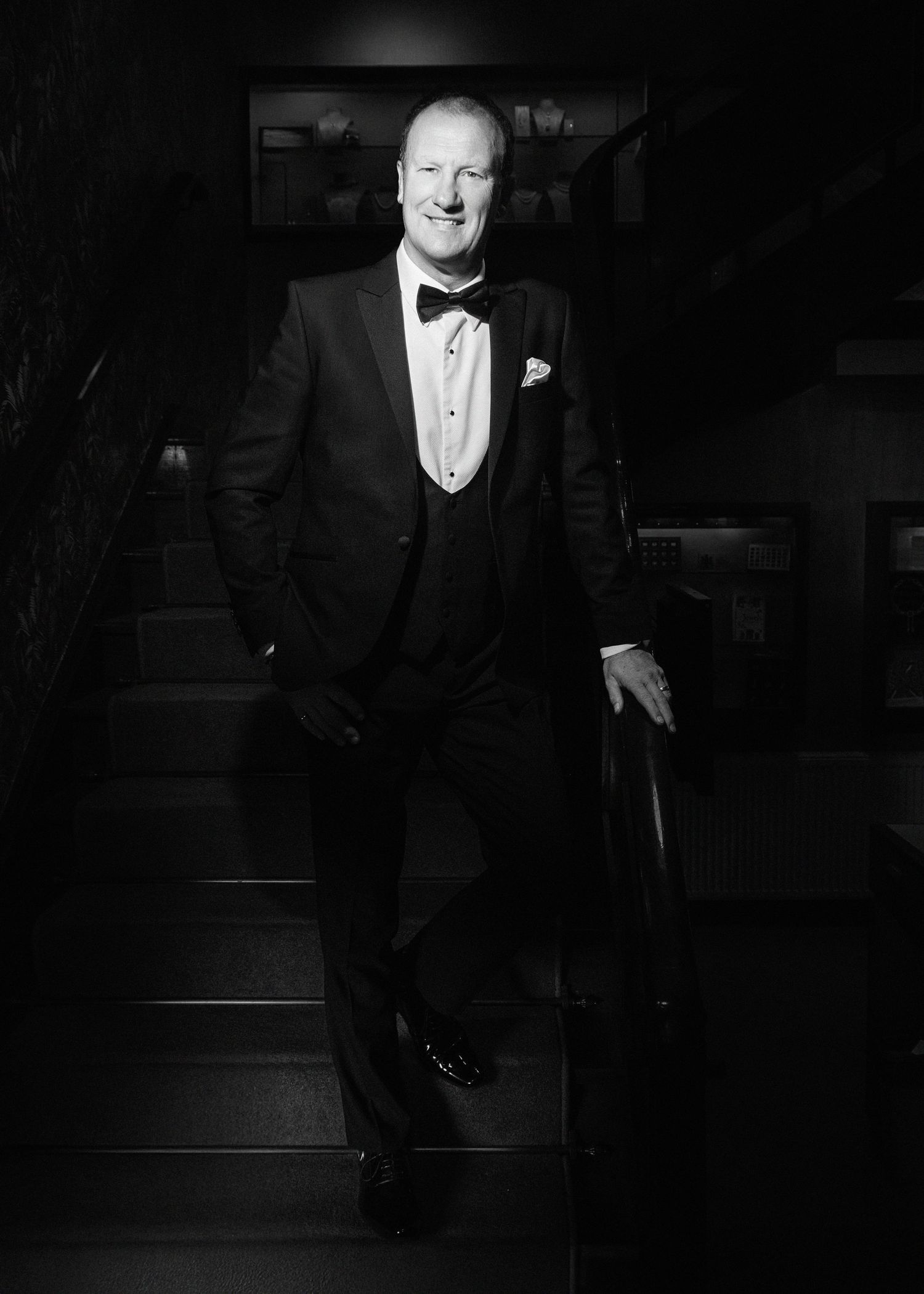 Dramatic black and white photo of a gentleman in tuxedo standing on stairs.