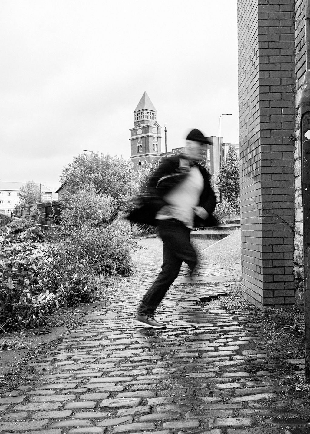 Blurred motion shot of a man running on a cobblestone path beside a brick wall with a tower behind.