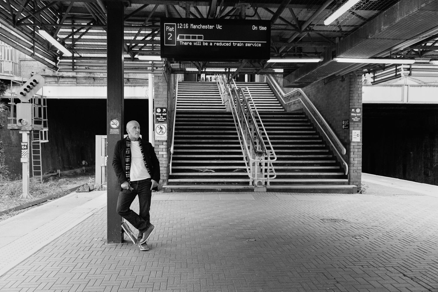 Black and white photograph of a train station platform with a large staircase and industrial architecture.