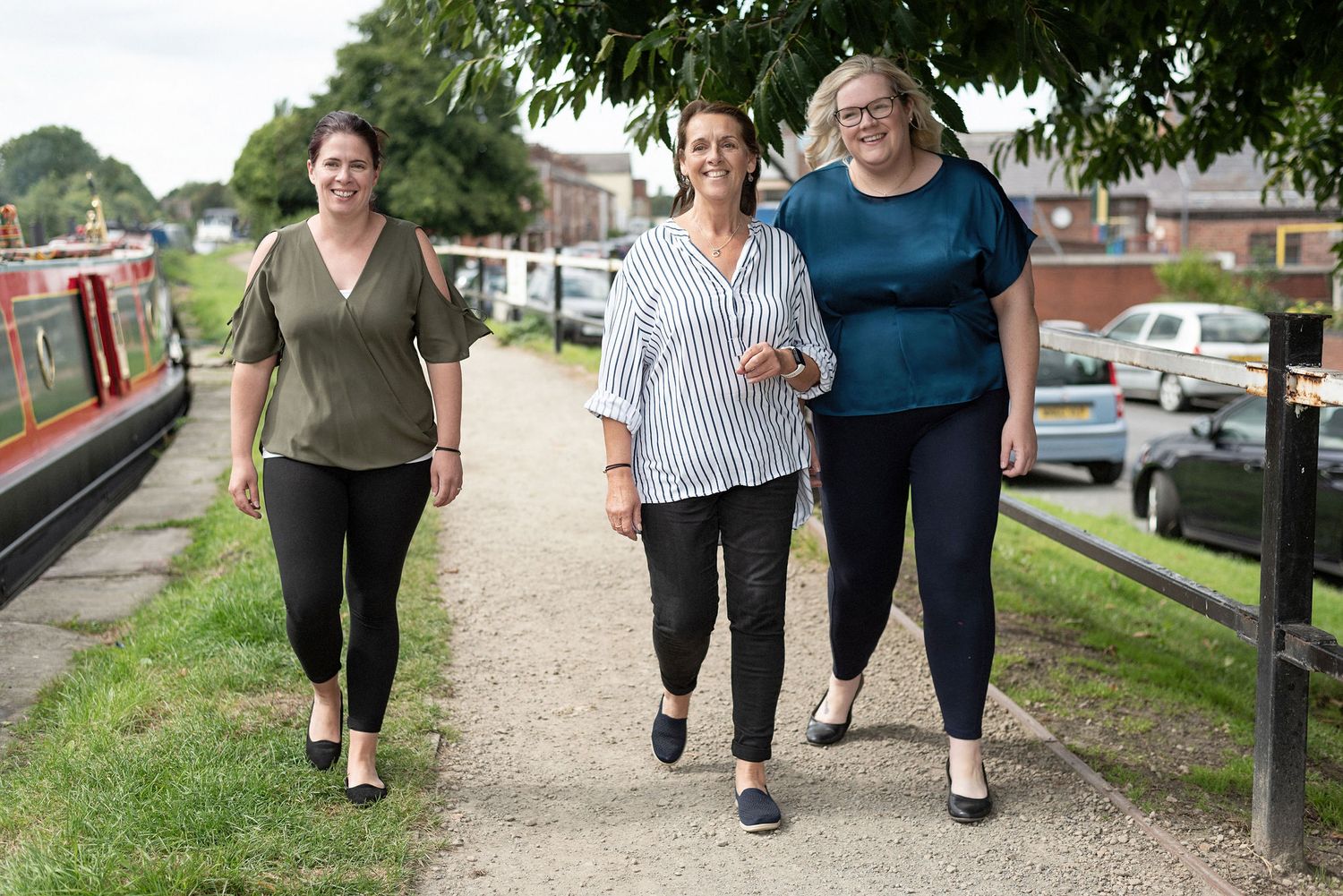 Three people walking together along canal path on sunny day.