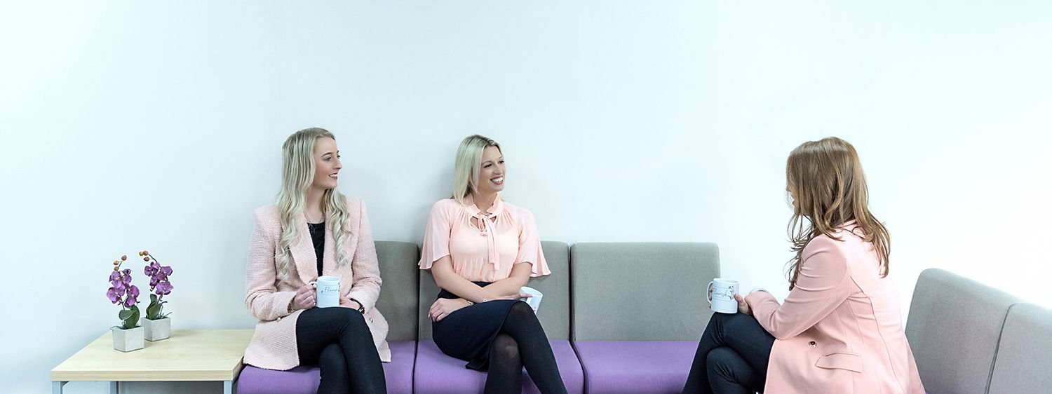 Three professionals sitting on a grey couch during a business meeting in a modern office setting.