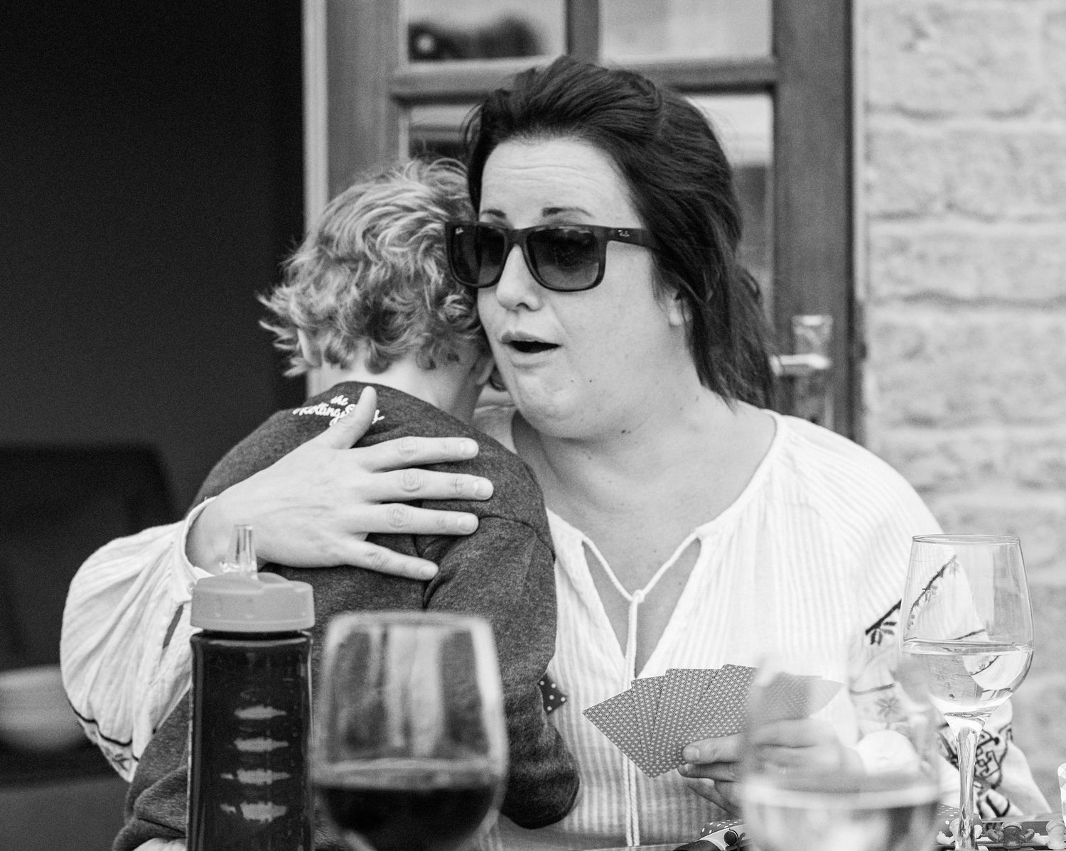 A person in sunglasses enjoys a drink at an outdoor cafe while engaging in conversation.