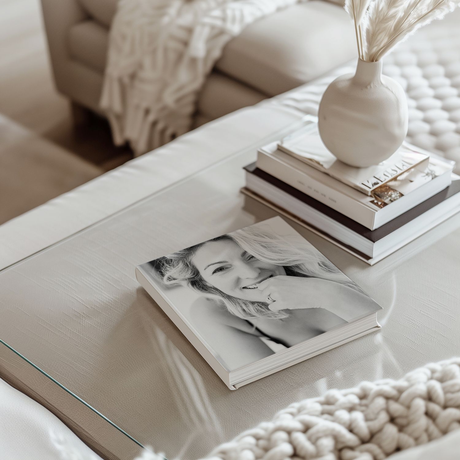 Minimalist coffee table styling with stacked books, a white ceramic vase, and black and white photography on white surface.
