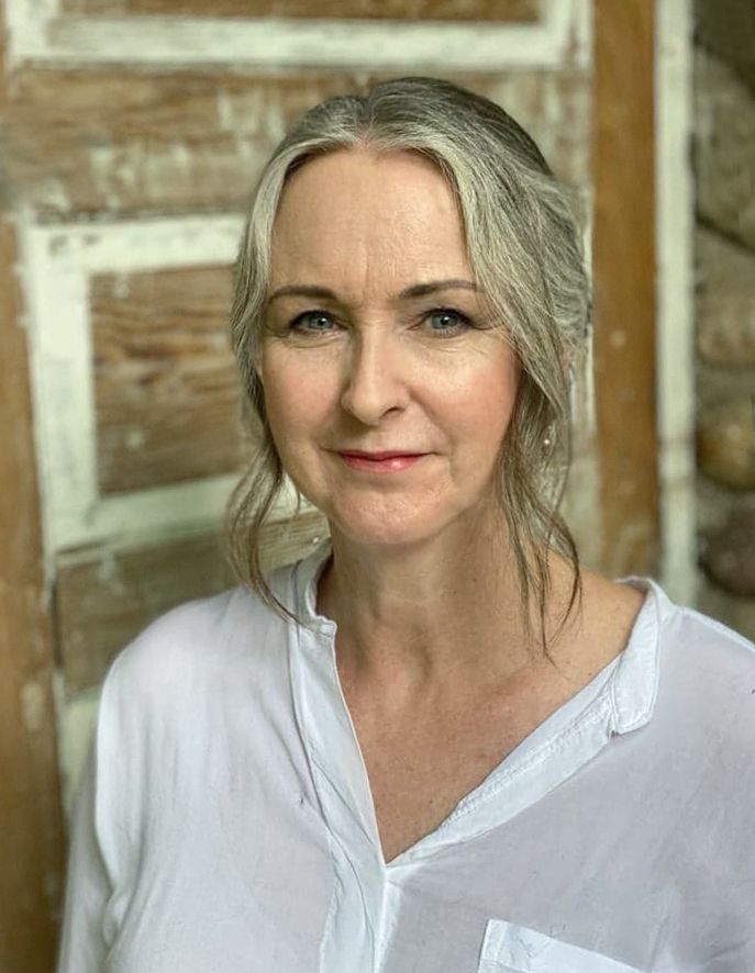 Portrait of a woman in a white shirt against a rustic wooden background.