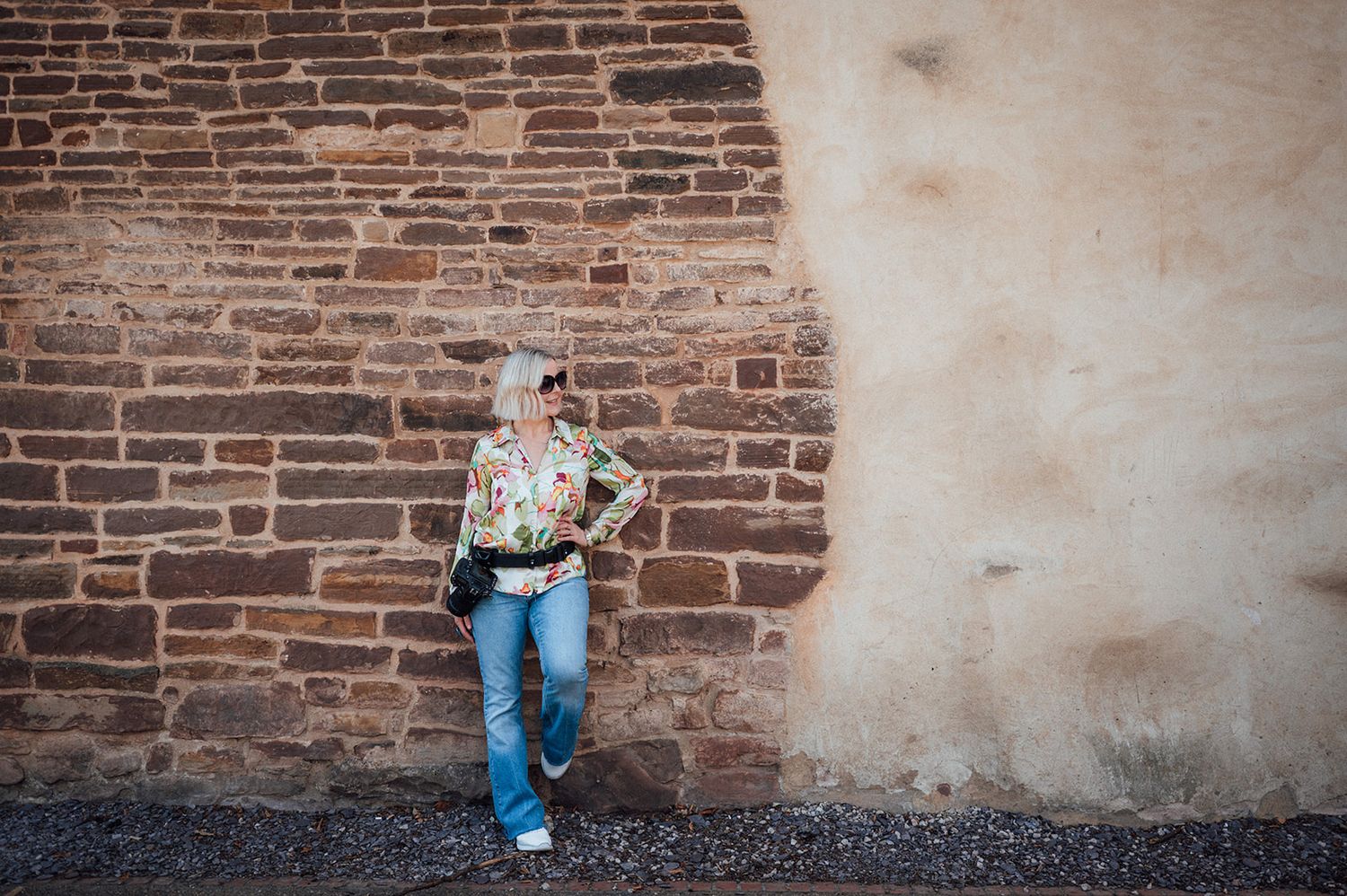 Person in casual attire leaning against rustic brick wall outdoors.