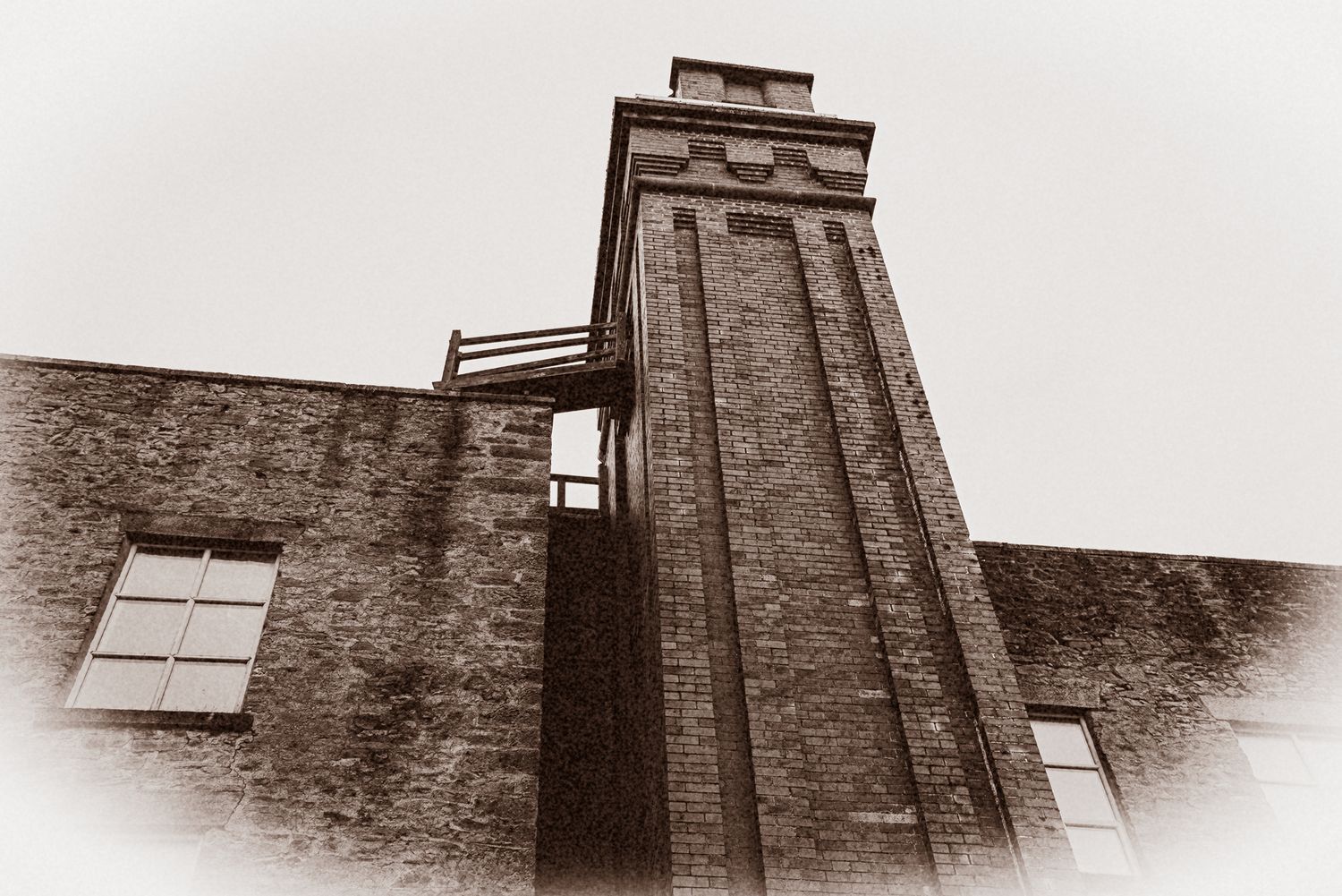 Sepia toned architectural image of tall industrial brick tower with windows.
