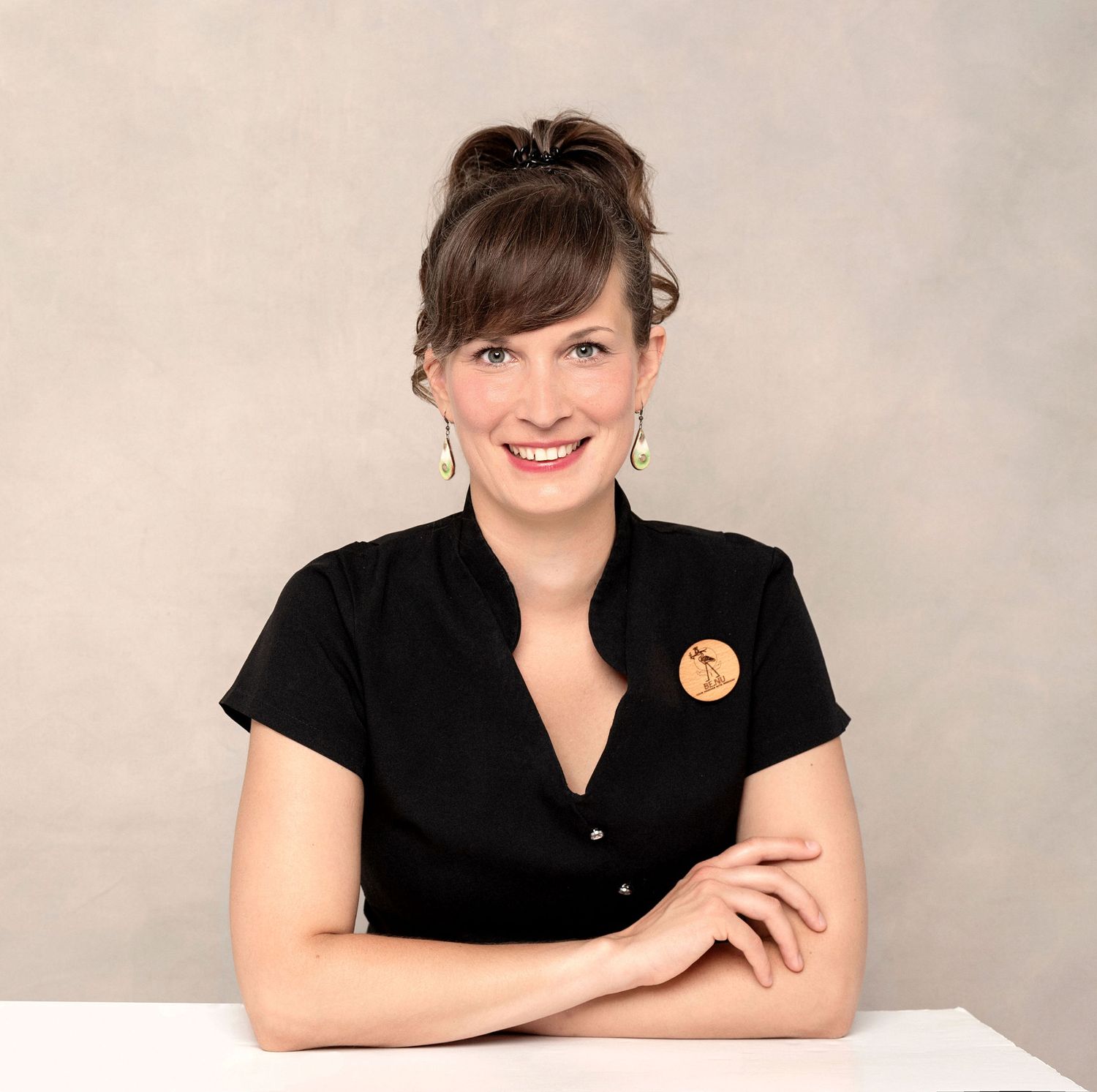 Professional portrait in black button-up shirt with decorative pin against neutral background.