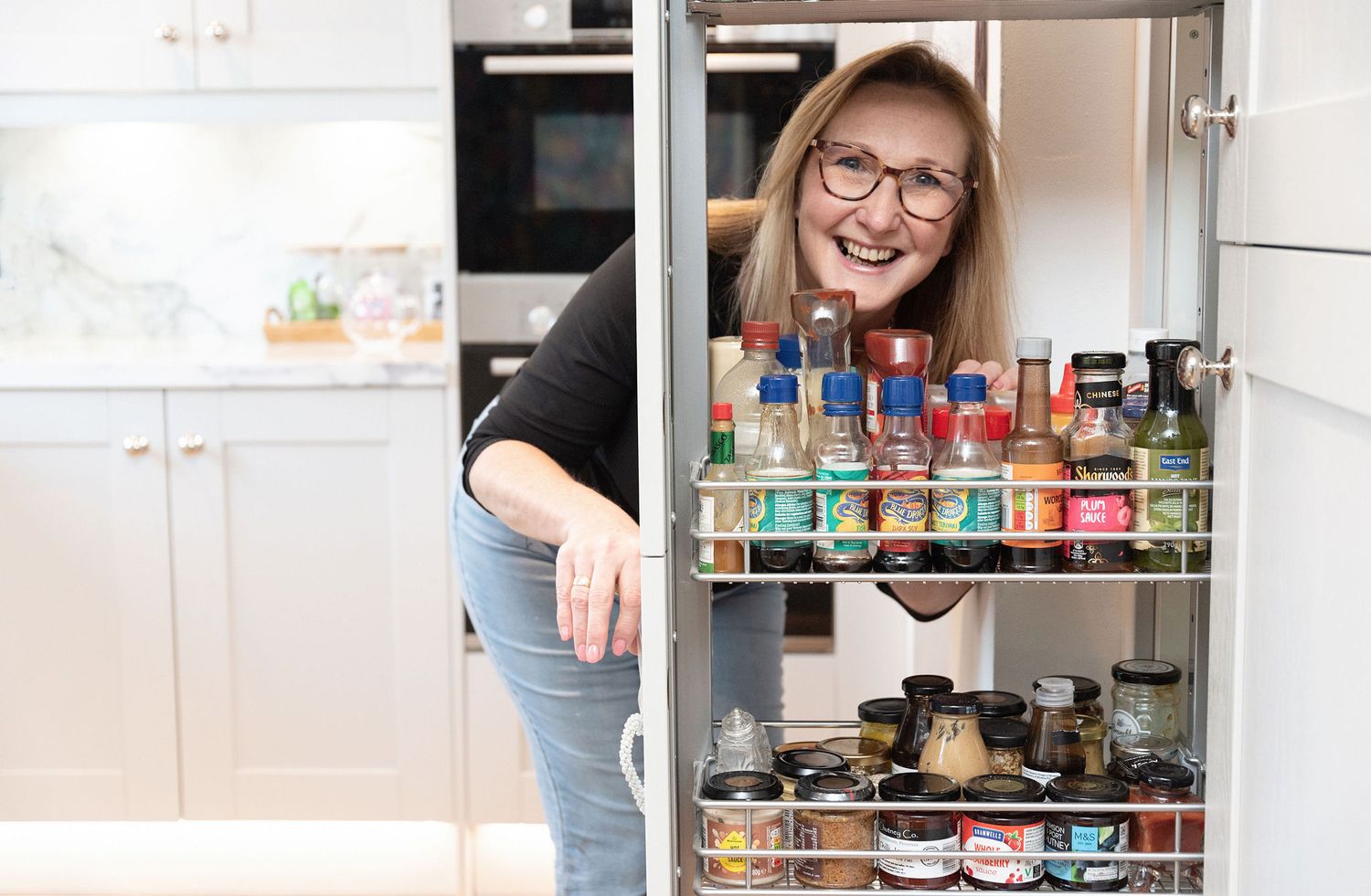 Woman looking through organized pantry shelves stocked with colorful spice containers.