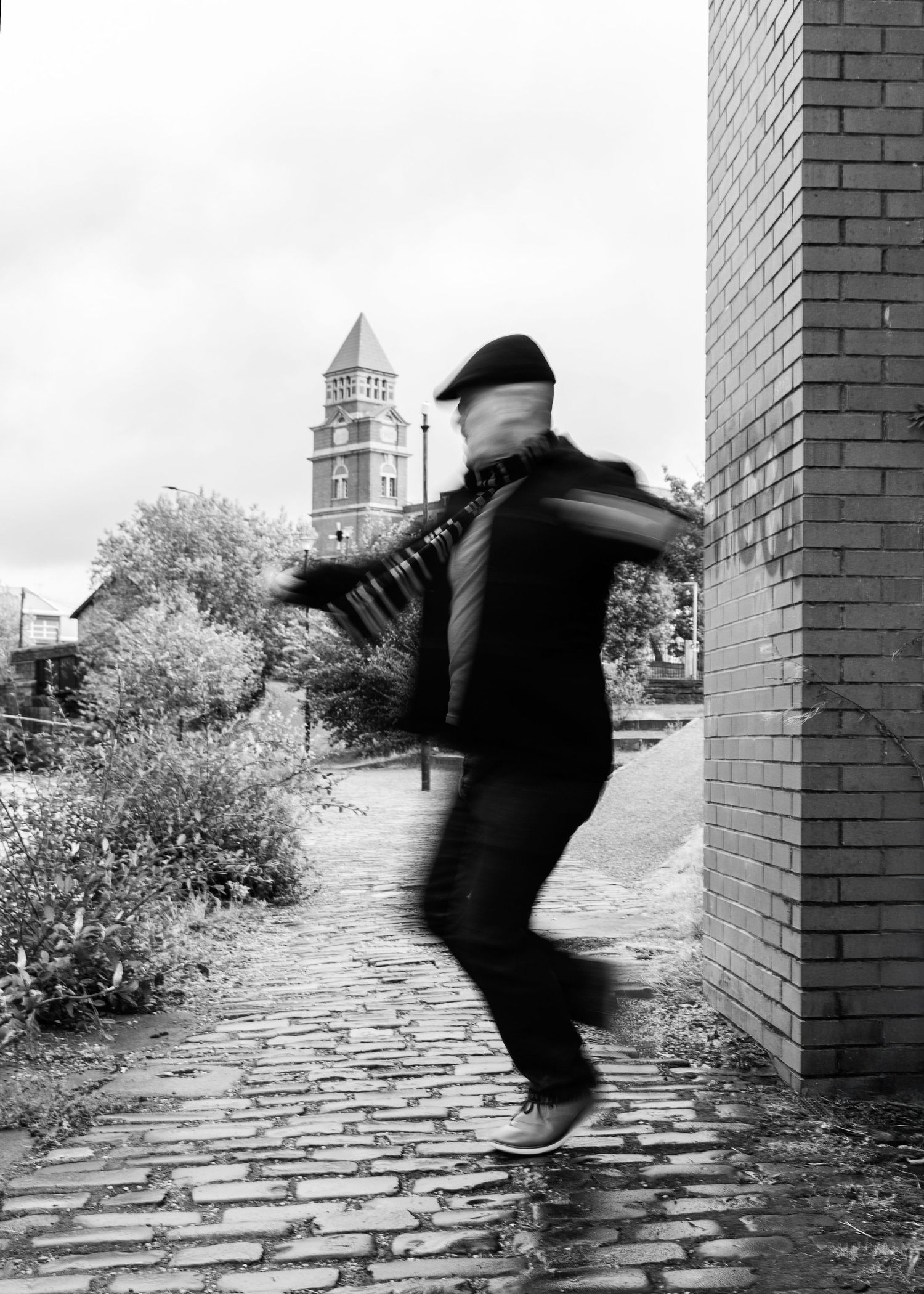 A person in a dark suit walks along a cobblestone street in a sequence of black and white photographs.