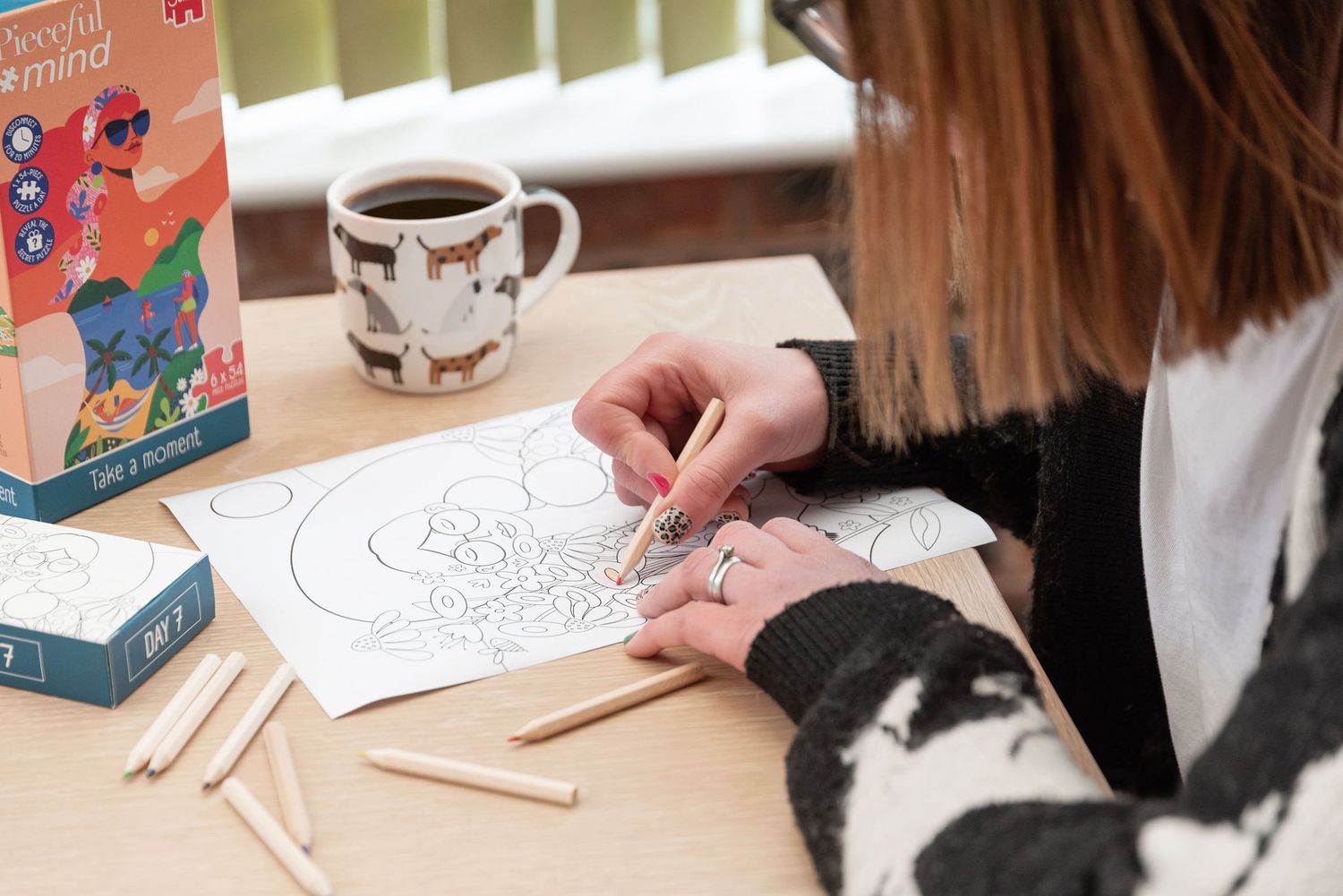 Someone coloring in an art book with colored pencils while enjoying coffee with a cat-themed mug on the table.
