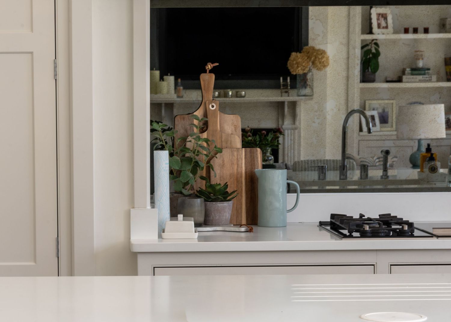 Modern white kitchen counter with wooden cutting boards, potted plant, blue mug, and gas stove near a window.