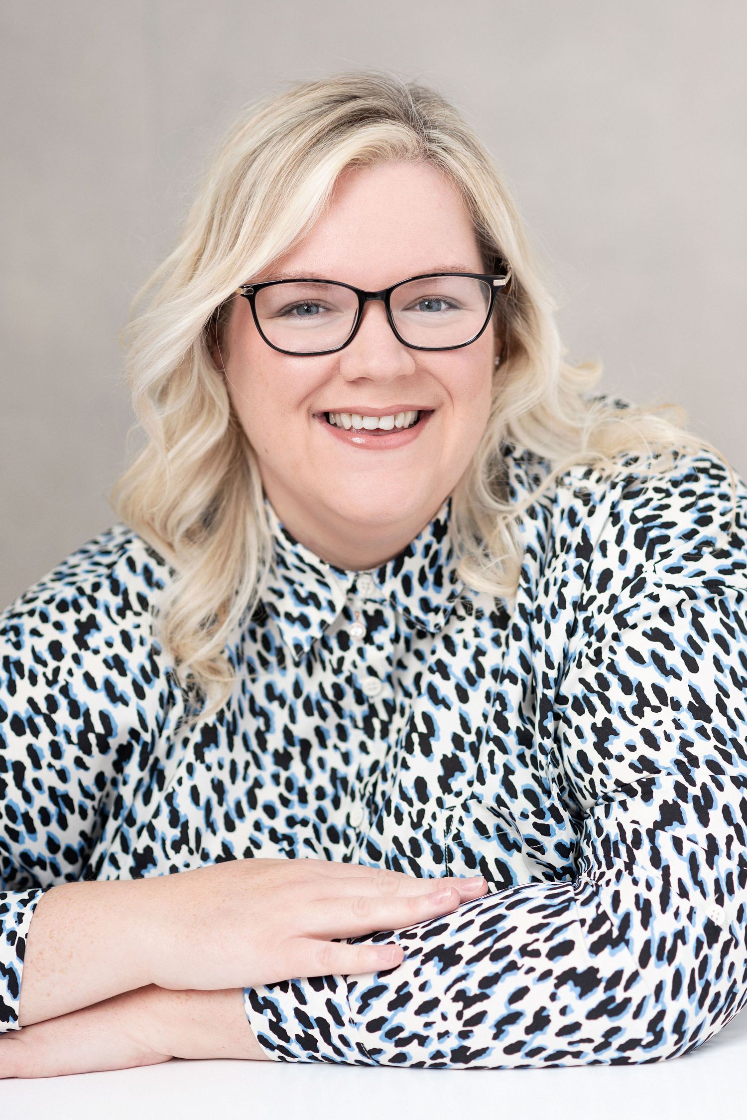 Studio portrait of person in animal print top wearing glasses against light background.
