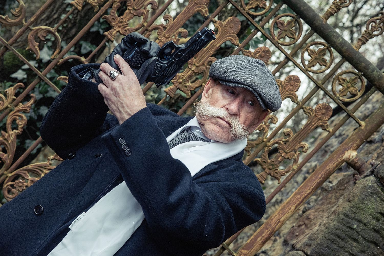Person in period clothing aims old-fashioned camera through ornate metal gate.