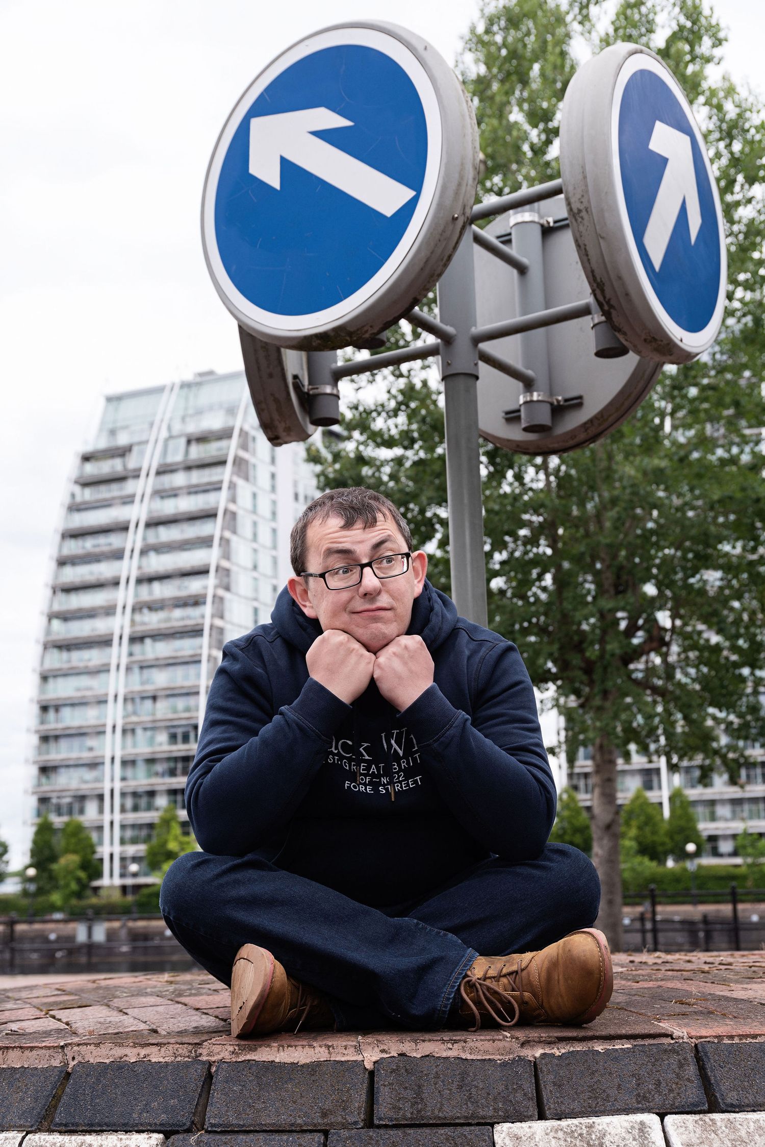Person sitting cross-legged under blue directional signs in urban setting.