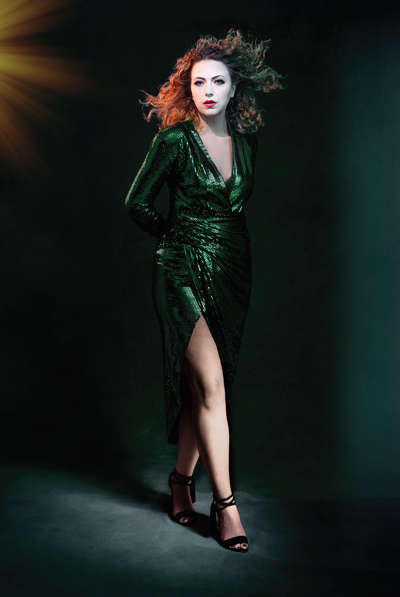 Fashion photo of a sparkly green evening gown with dramatic lighting and wind-blown hair.