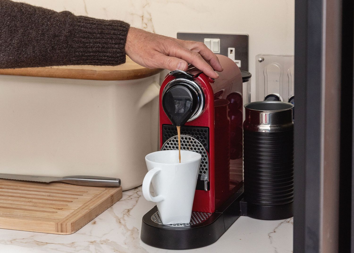 A modern red and black coffee maker sits on a white countertop with coffee accessories nearby.