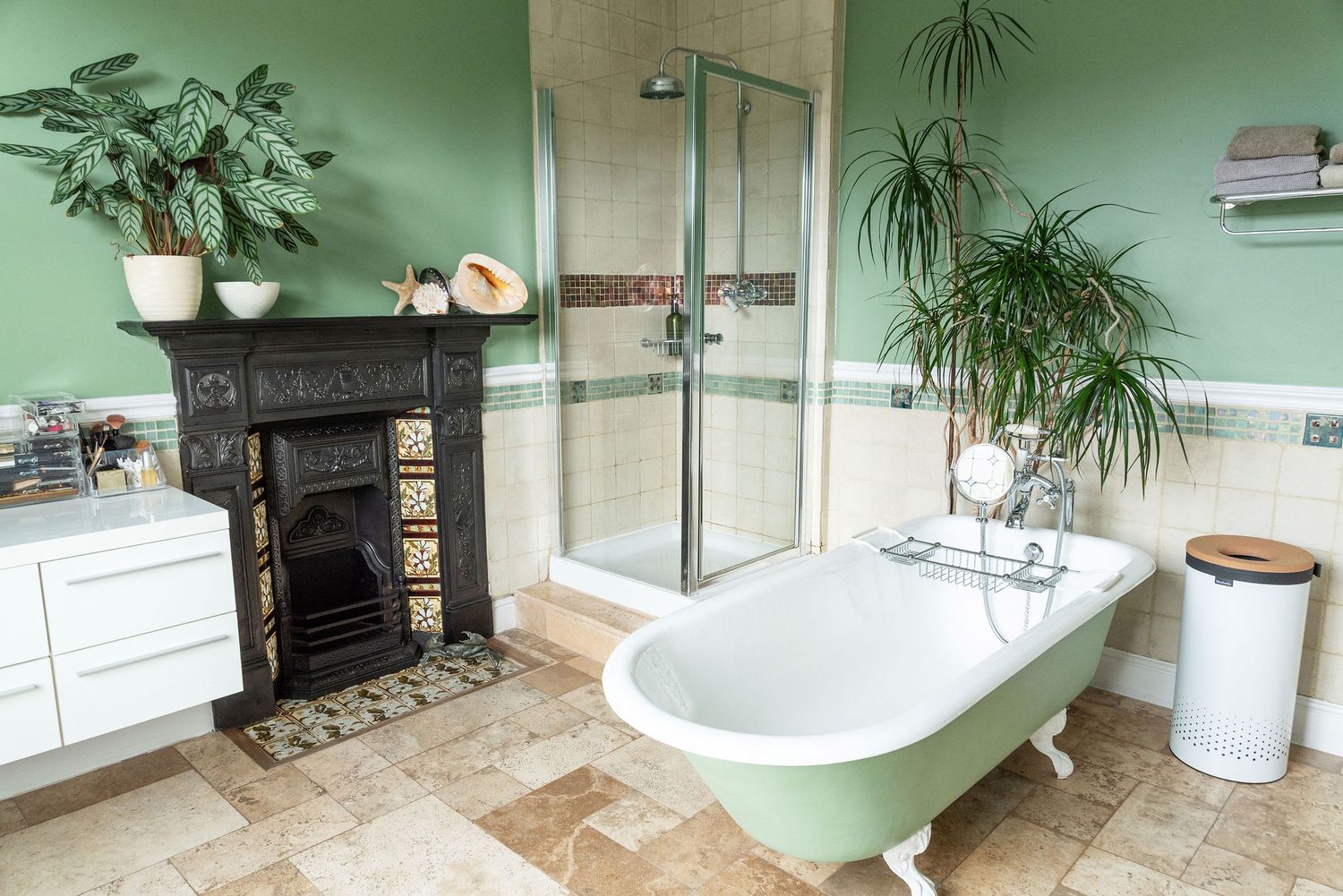 Modern bathroom with mint green walls, stone tile flooring, freestanding tub and large windows overlooking nature.