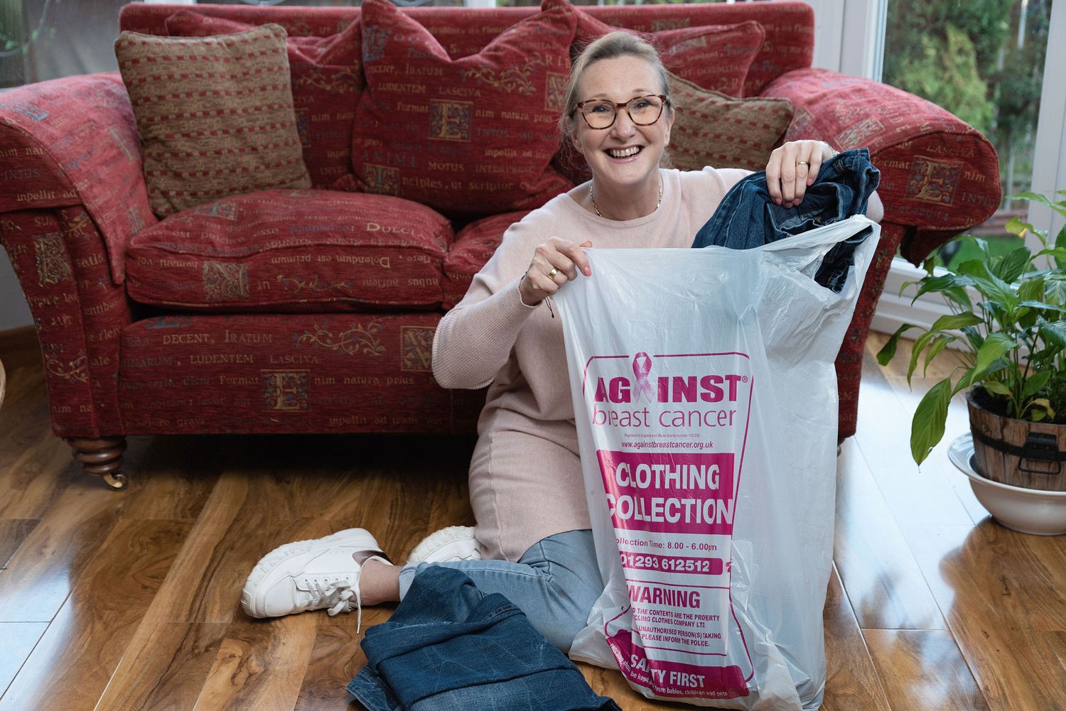 Person displaying cleaning supplies and laundry bag while sitting on red couch.