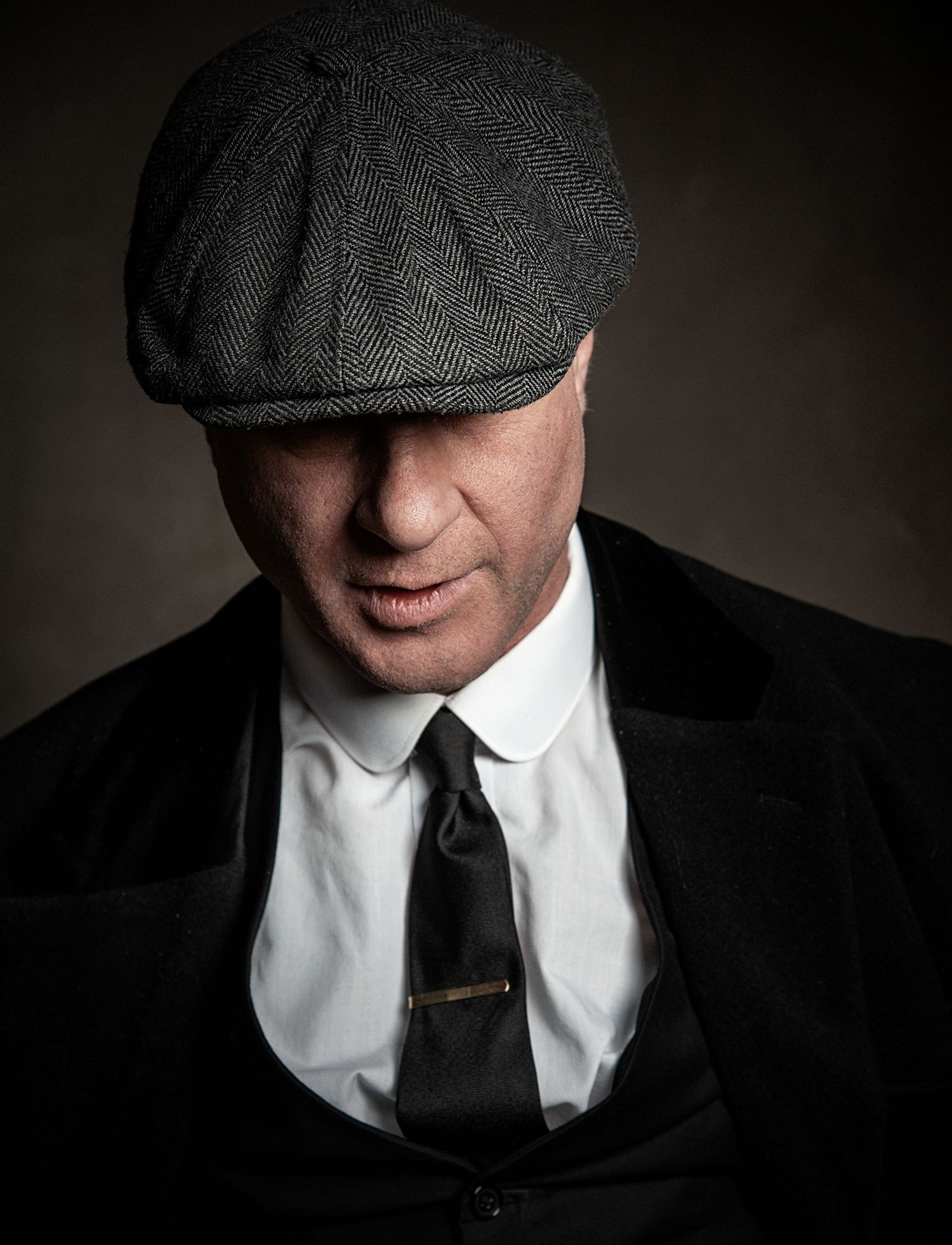 Dramatic portrait of person in flat cap and suit tie with moody lighting.