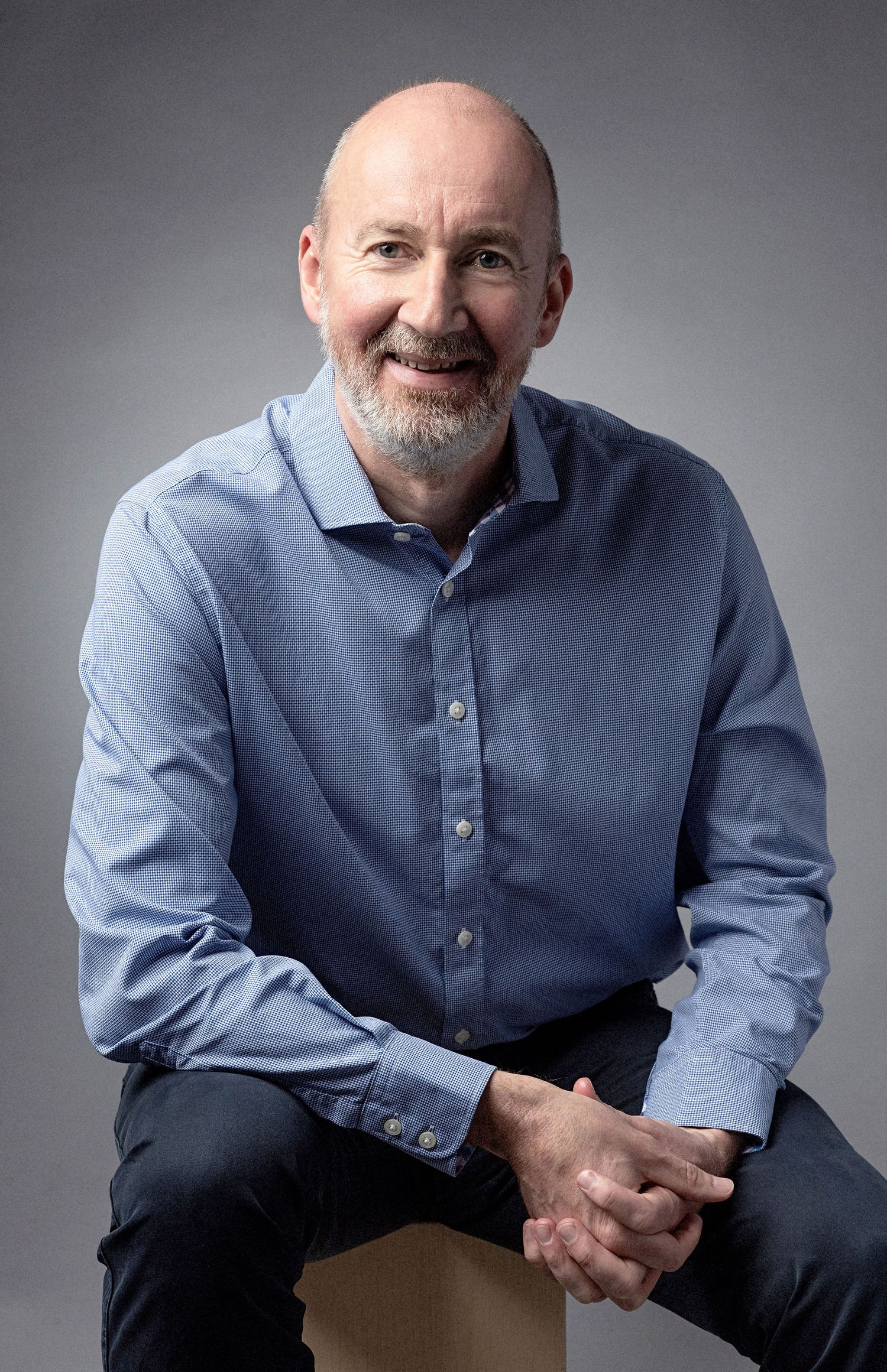 Studio portrait of a person in blue button-down shirt against grey backdrop.