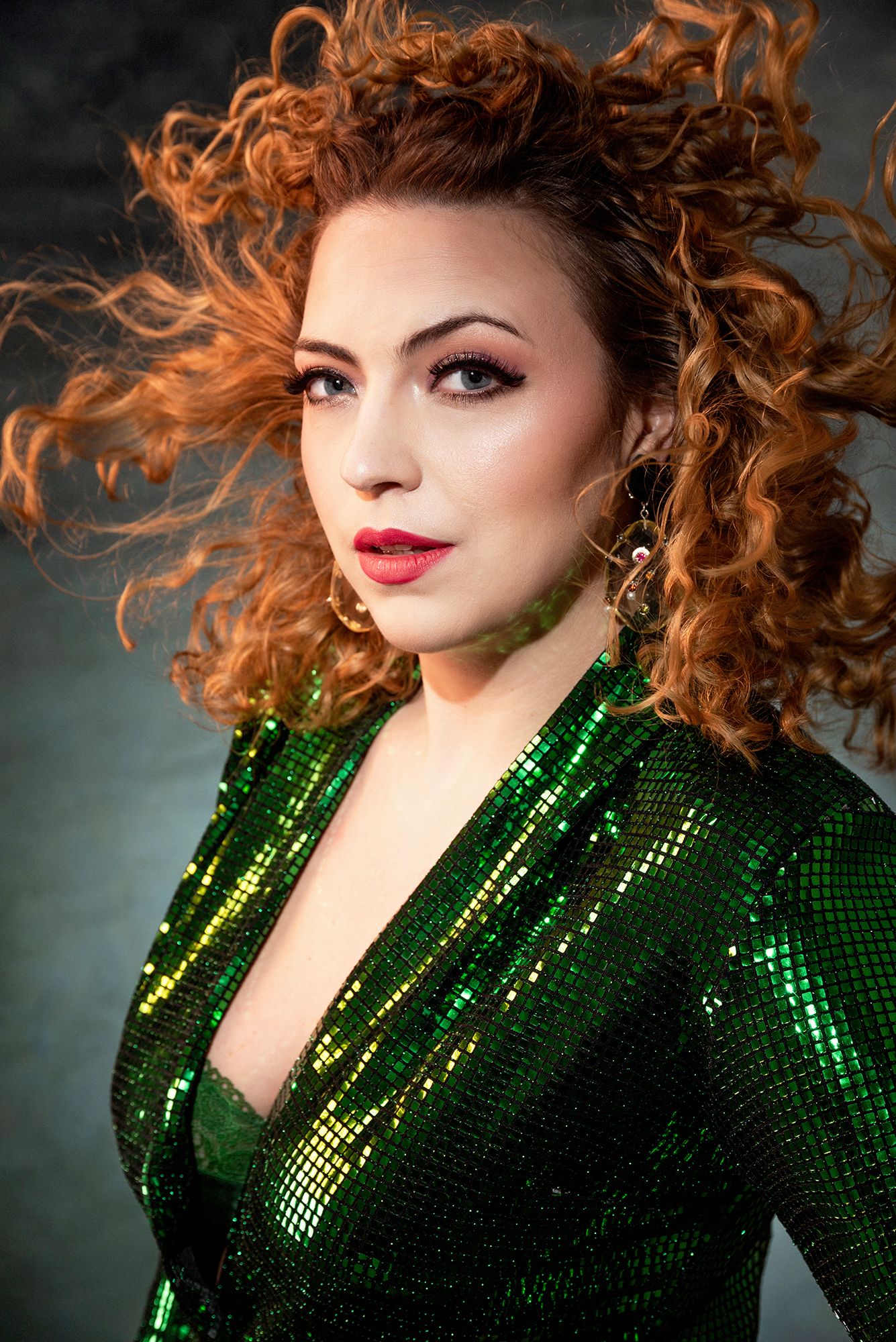 A glamour shot featuring curly red hair and an emerald sequined dress against a dark background.