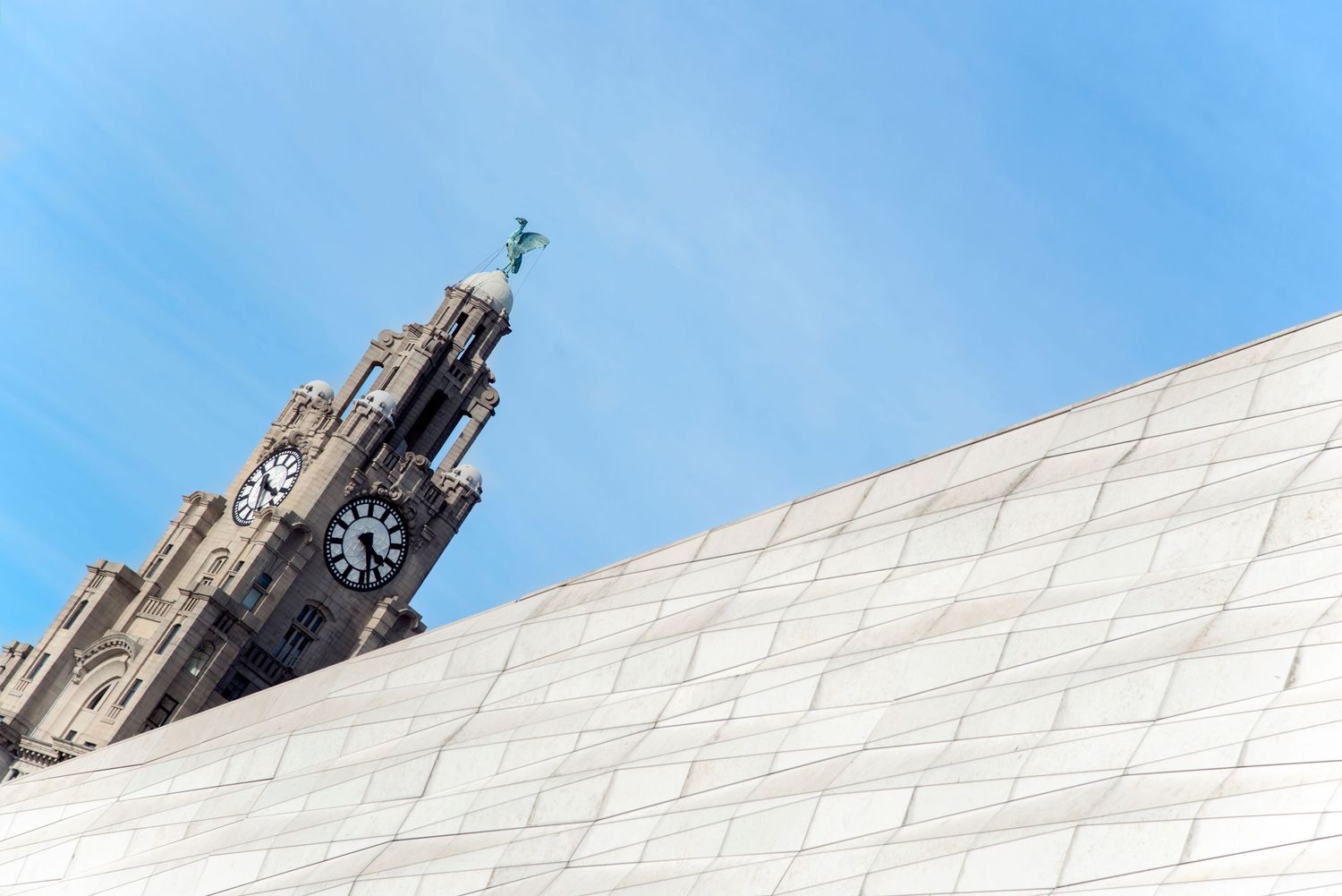 Royal Liver Building clock tower rising above a modern white marble facade against a blue sky in Liverpool.