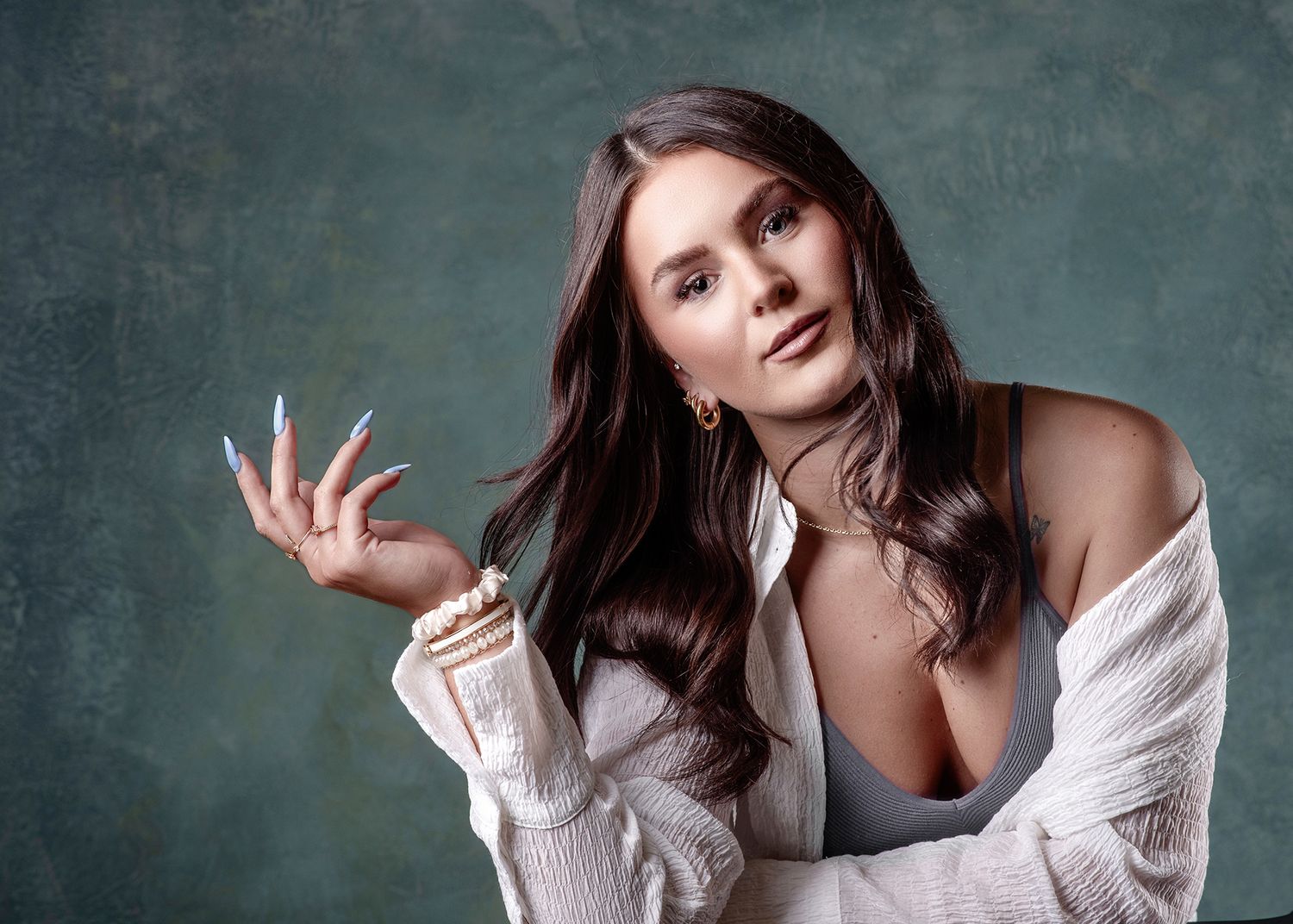 A person with long dark hair poses against a teal backdrop in a series of artistic fashion portraits.