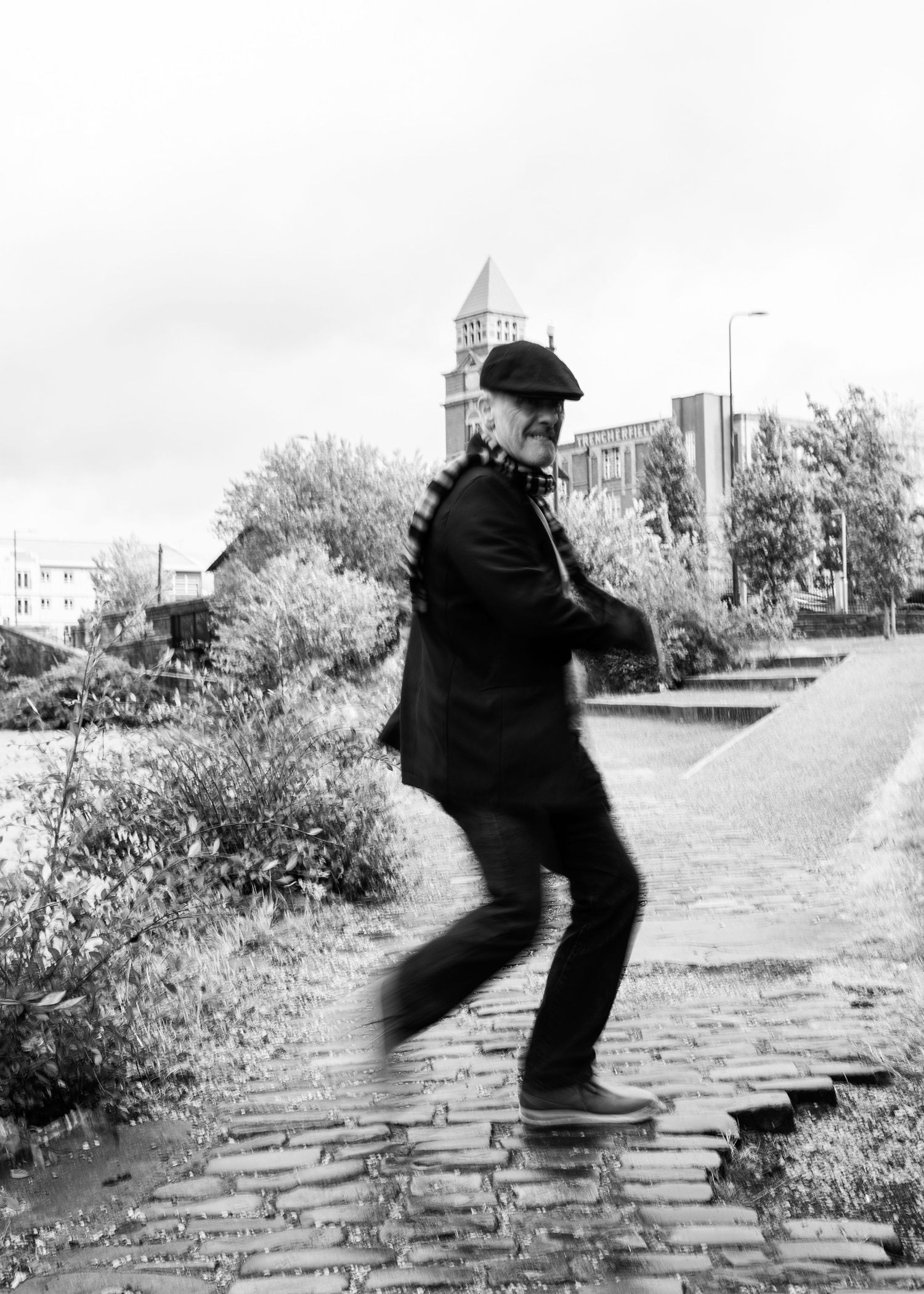 A sequence of black and white photos showing a figure jumping across cobblestones in an urban setting.