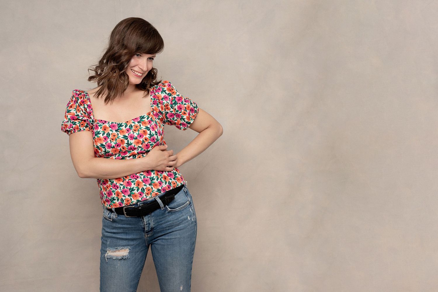 Casual pose against beige wall wearing floral print top and distressed jeans.