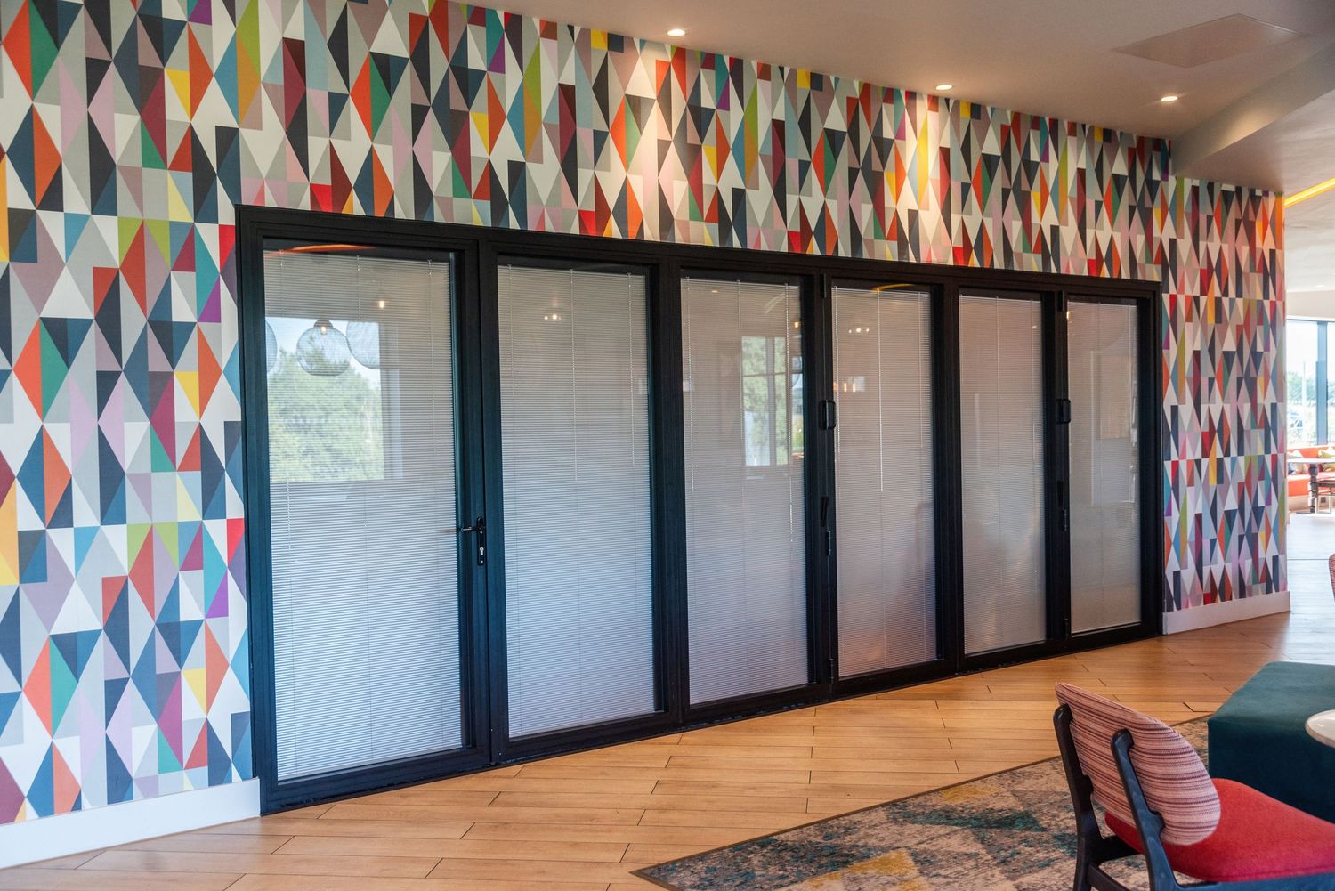 Hotel hallway with black doors and colorful geometric patterned wallpaper.