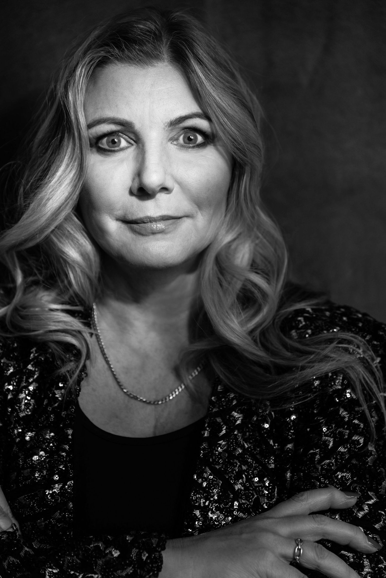Professional black and white headshot featuring wavy hair and a sparkling evening jacket.