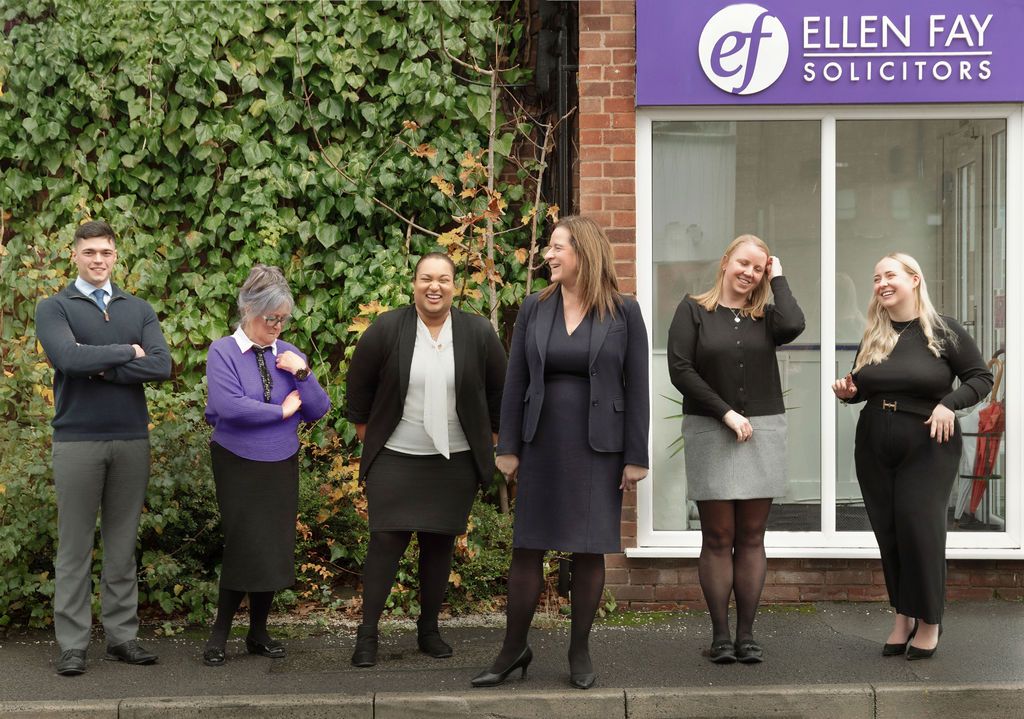 A group of business professionals in suits pose outside an Ellen Fay Solicitors office building.