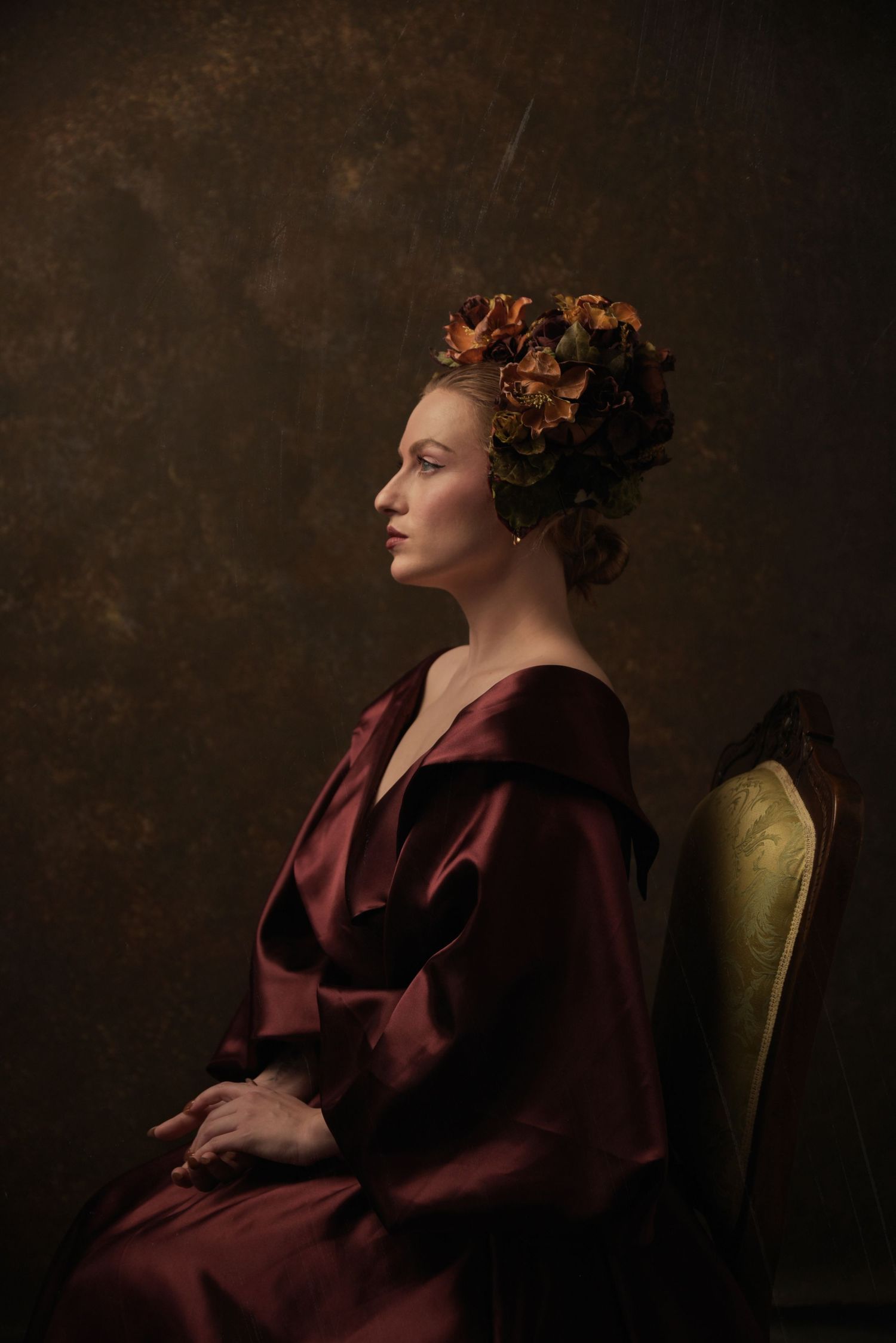 Classical portrait in burgundy dress with floral hair accessories in Renaissance style.