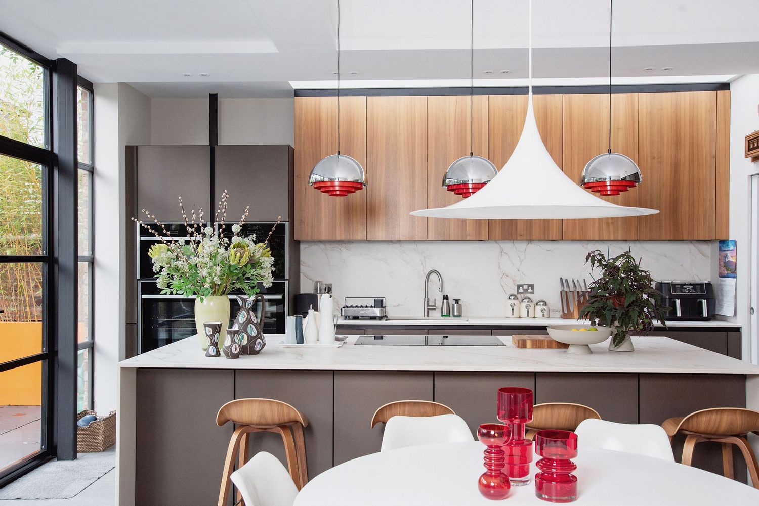 Modern kitchen features white pendant lights, wood cabinetry, and a sleek island with integrated dining space.