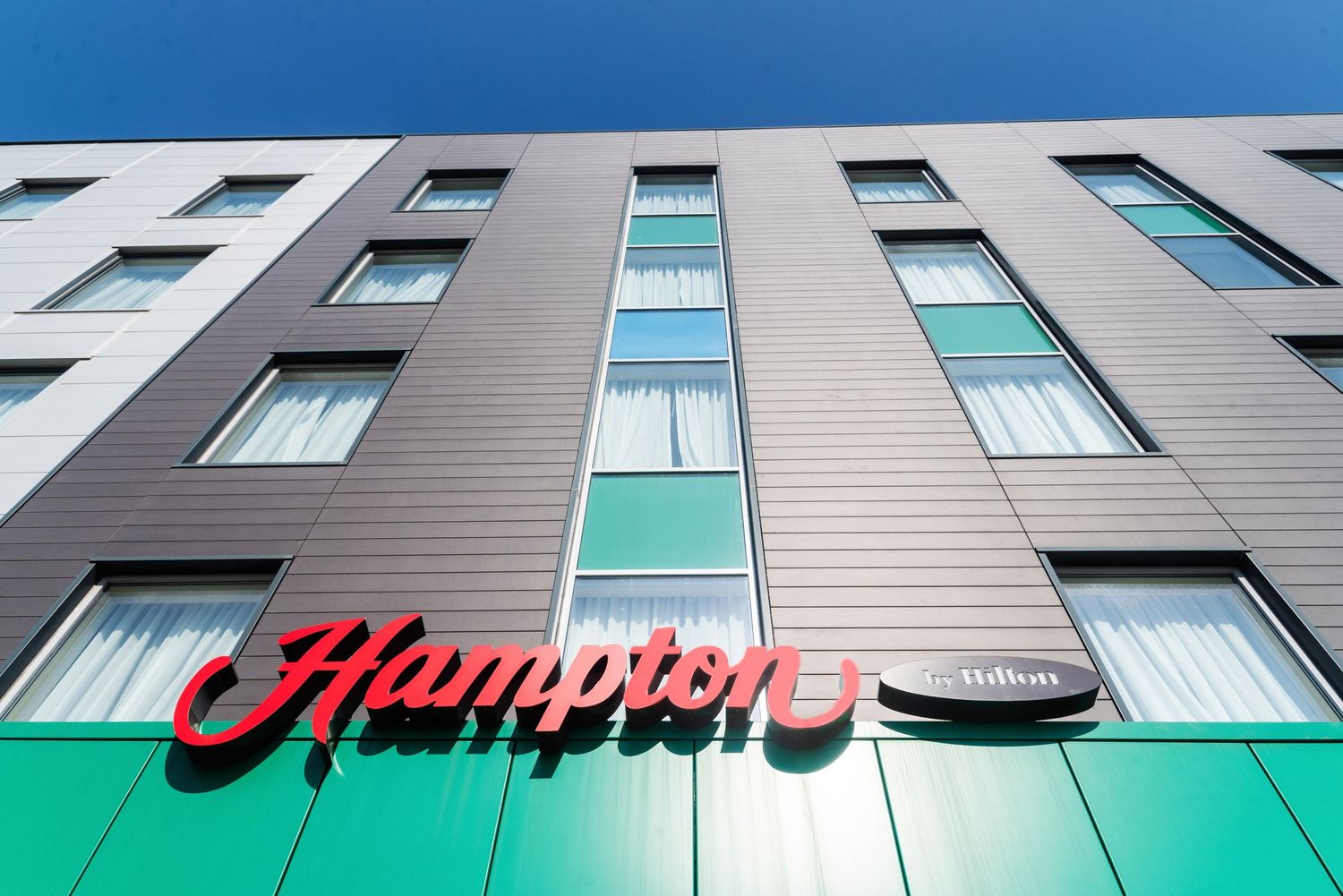 Modern Hampton hotel exterior facade with blue windows and green accent wall.