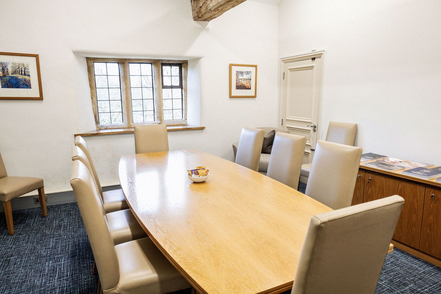 Modern conference room with wooden table and cream chairs under a beamed ceiling.