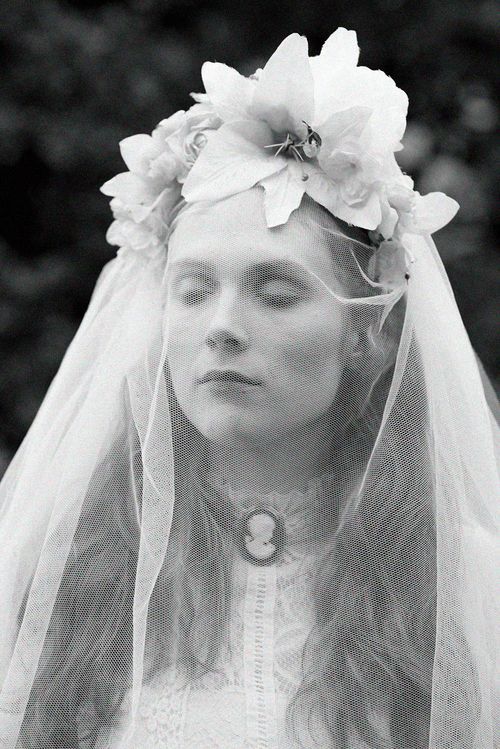 Black and white portrait of a bride wearing a floral crown and veil with a cameo necklace, eyes closed.