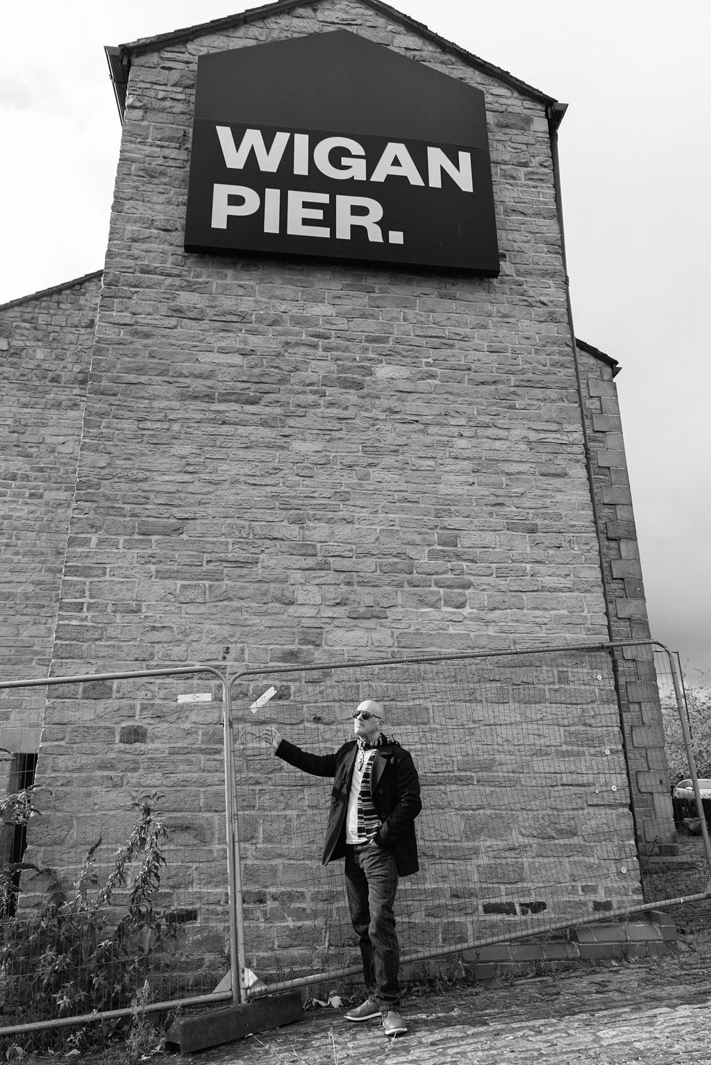 Black and white photo of a person standing outside the historic Wigan Pier brick building in Wigan, England.