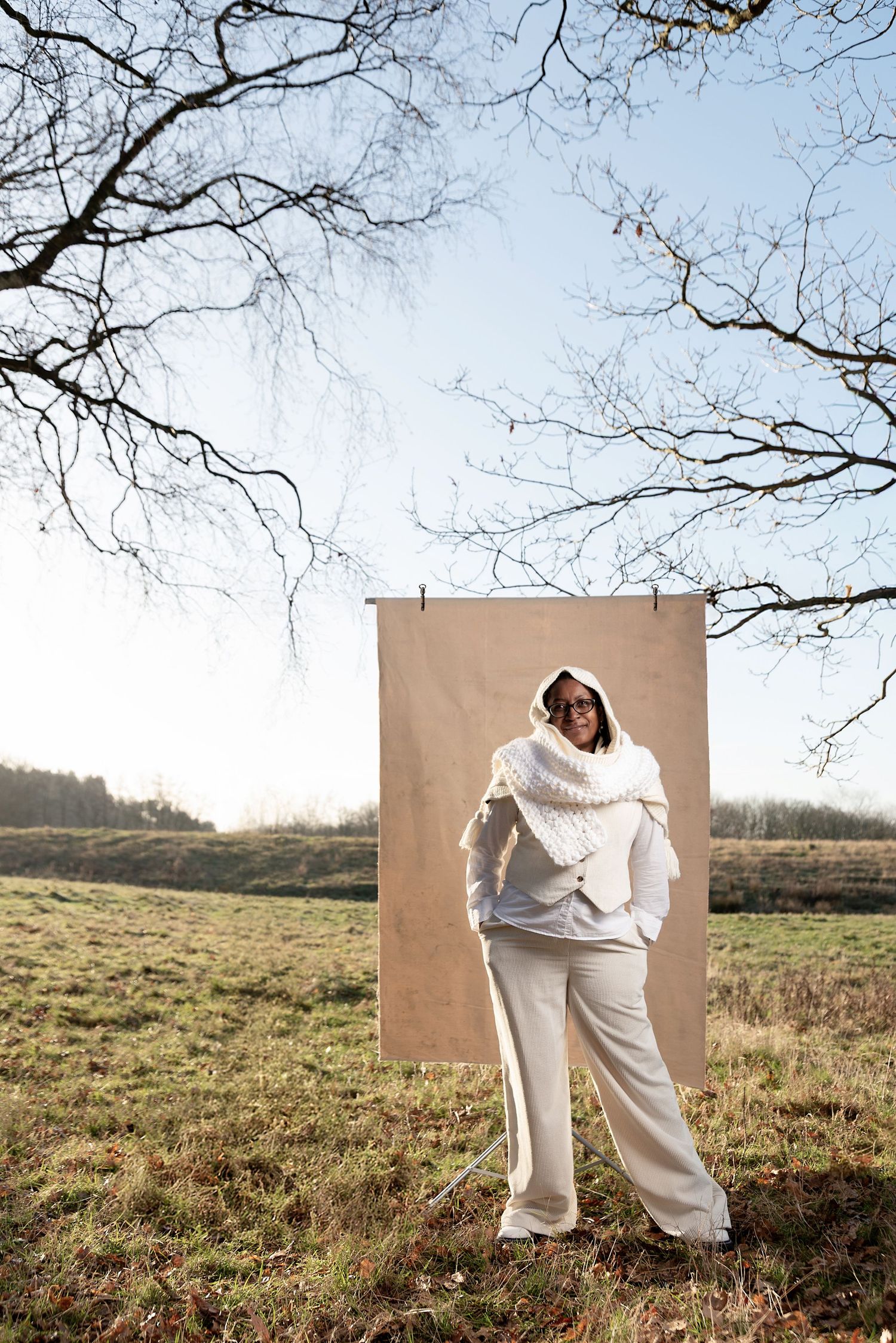 Fashion photography in a field showing a cream colored outfit against a tan backdrop with bare tree branches overhead.
