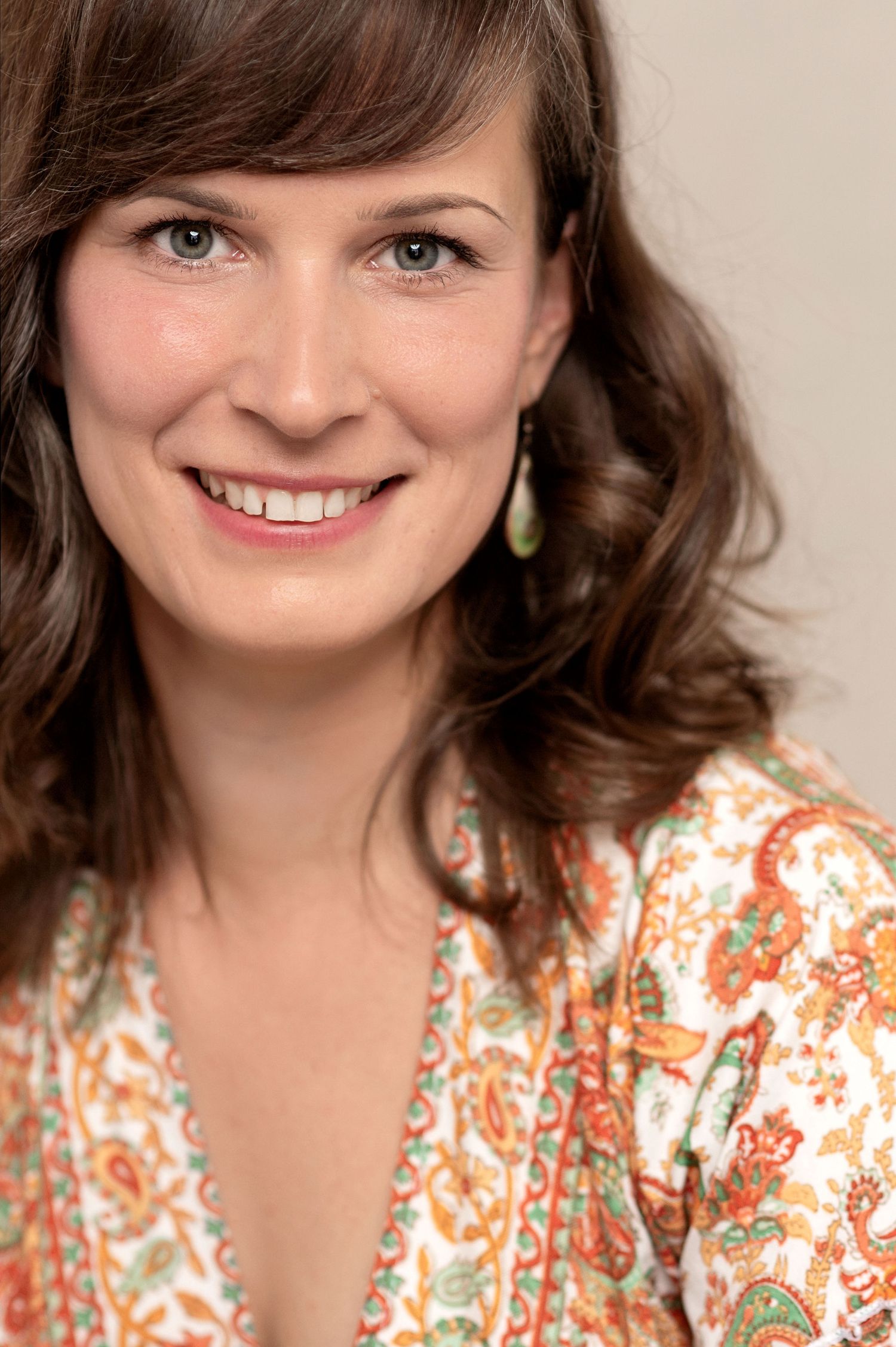 Portrait showing warm smile and side-swept bangs against neutral background wearing a patterned top.