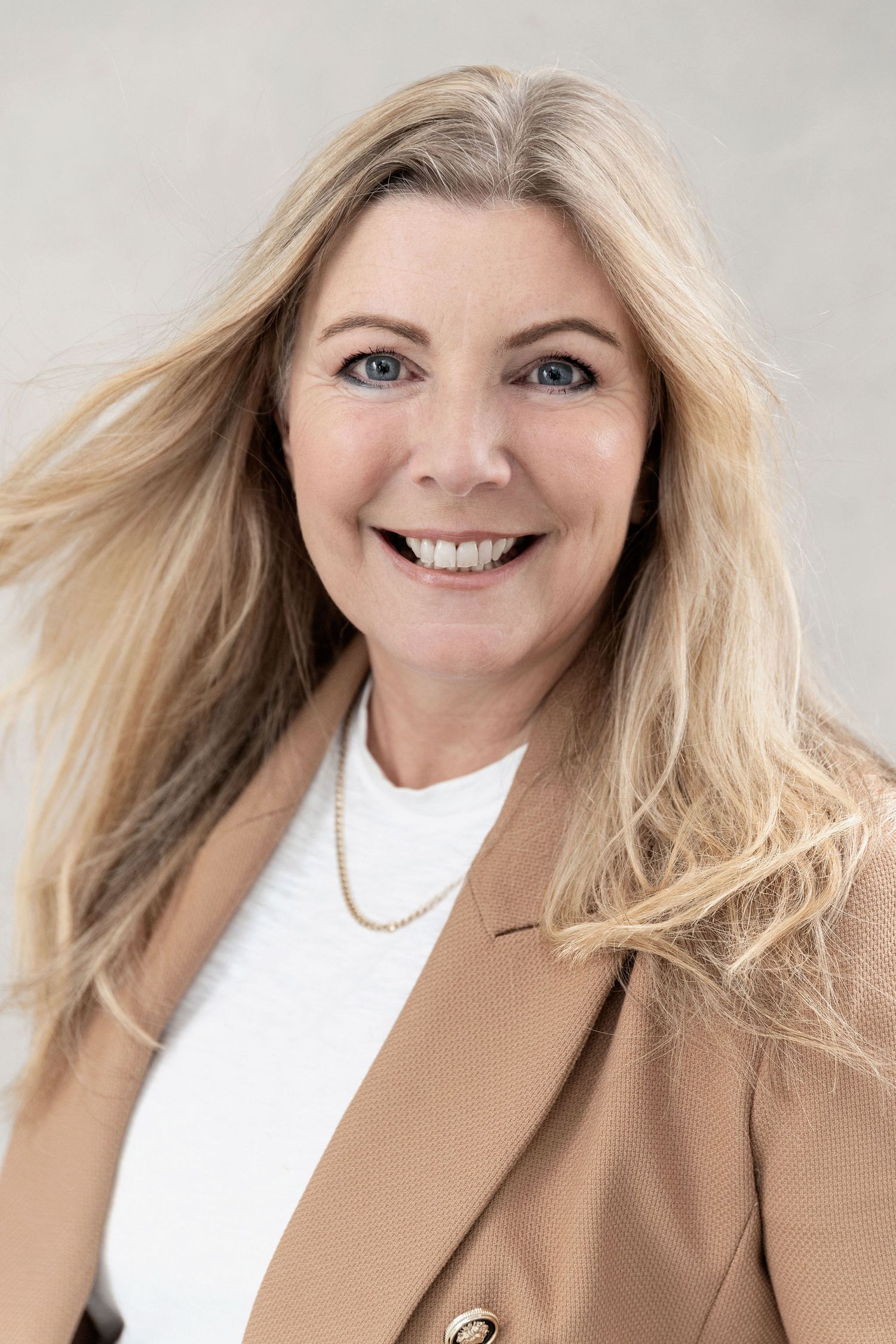 Professional headshot of someone in a tan blazer and white top against a light background.