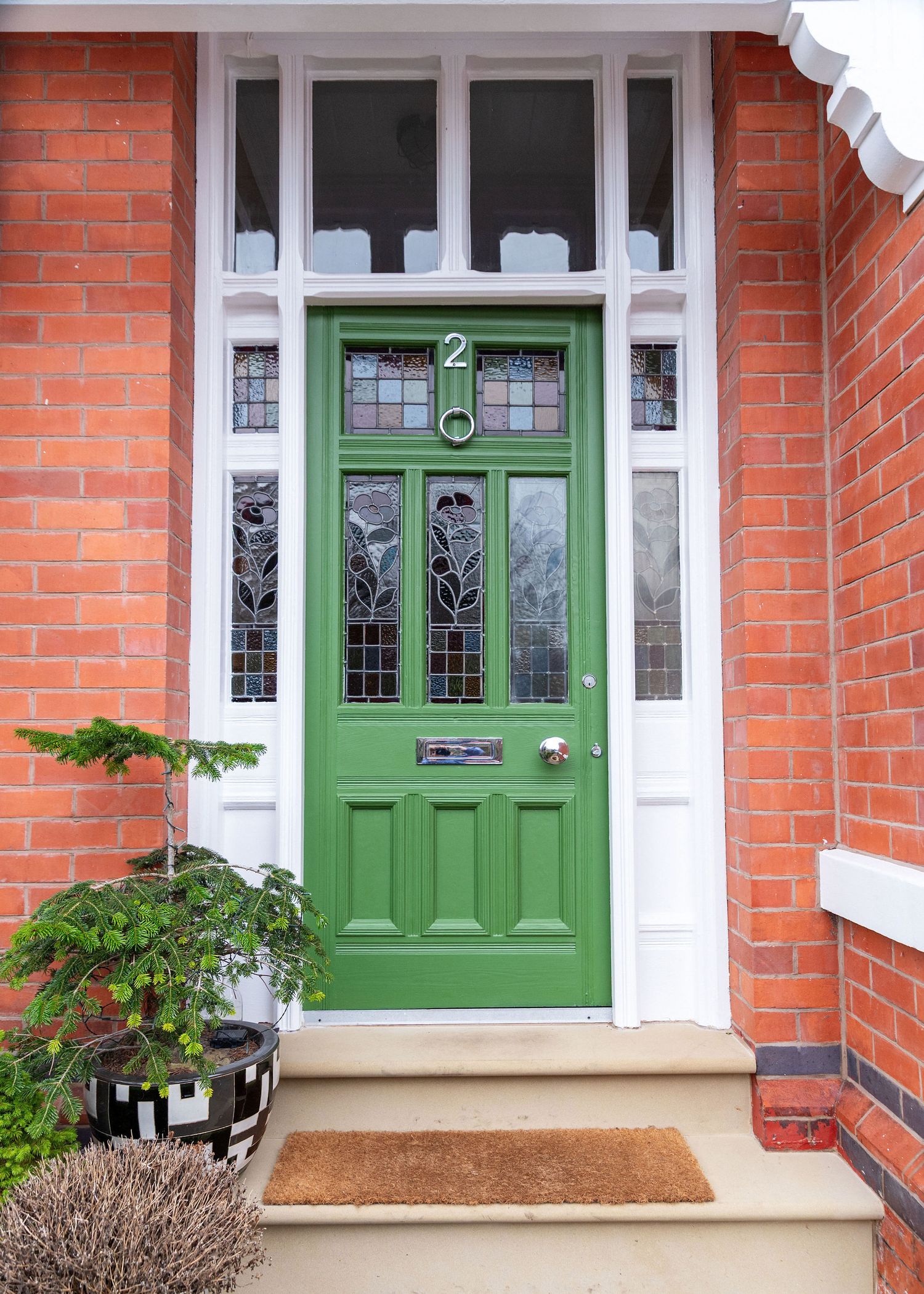 Green Victorian front door with white trim and sidelights on a red brick house with a concrete step entrance.